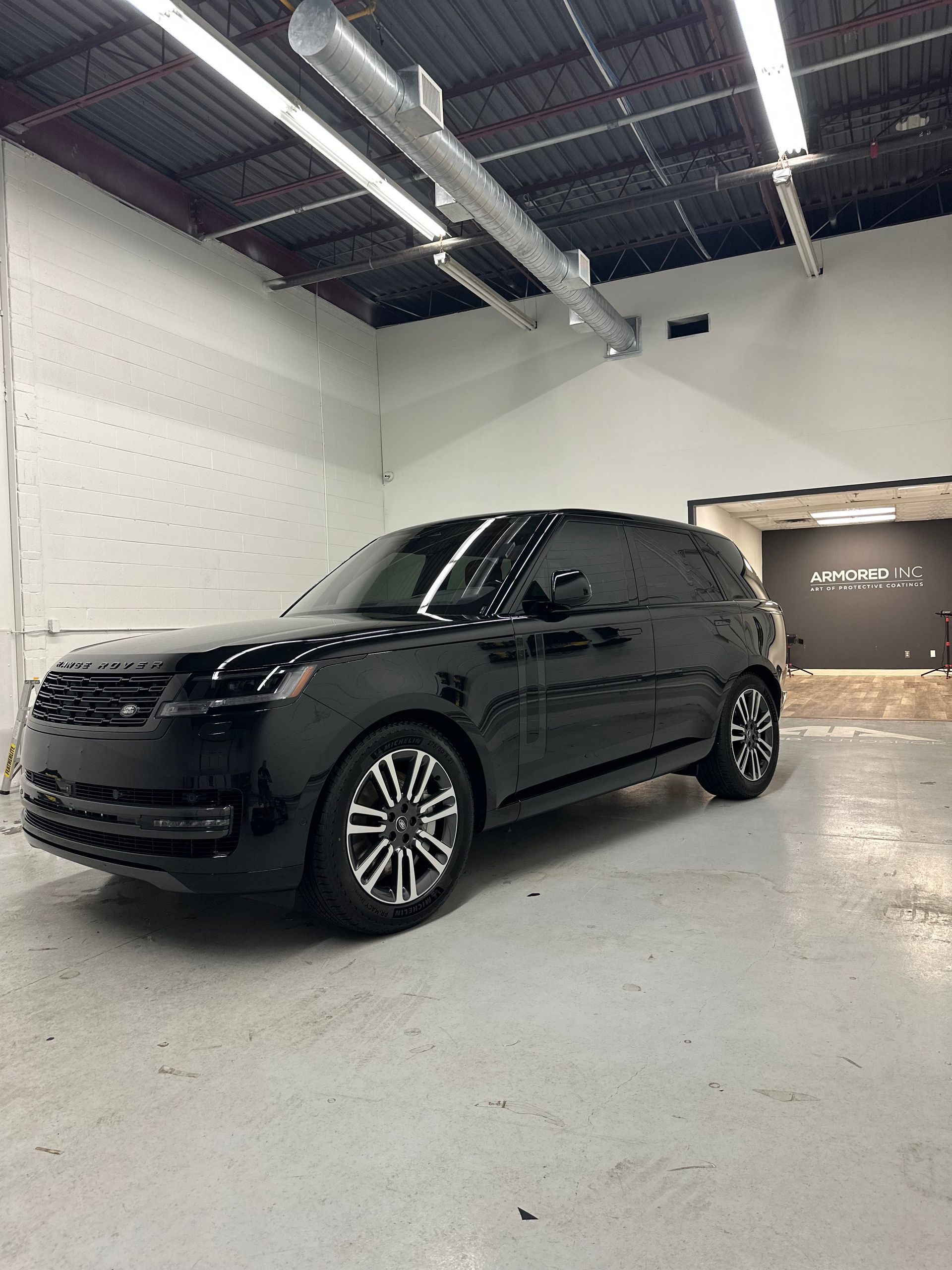 A black Range Rover parked in a brightly lit, white-walled garage with an exposed ceiling and industrial ductwork.