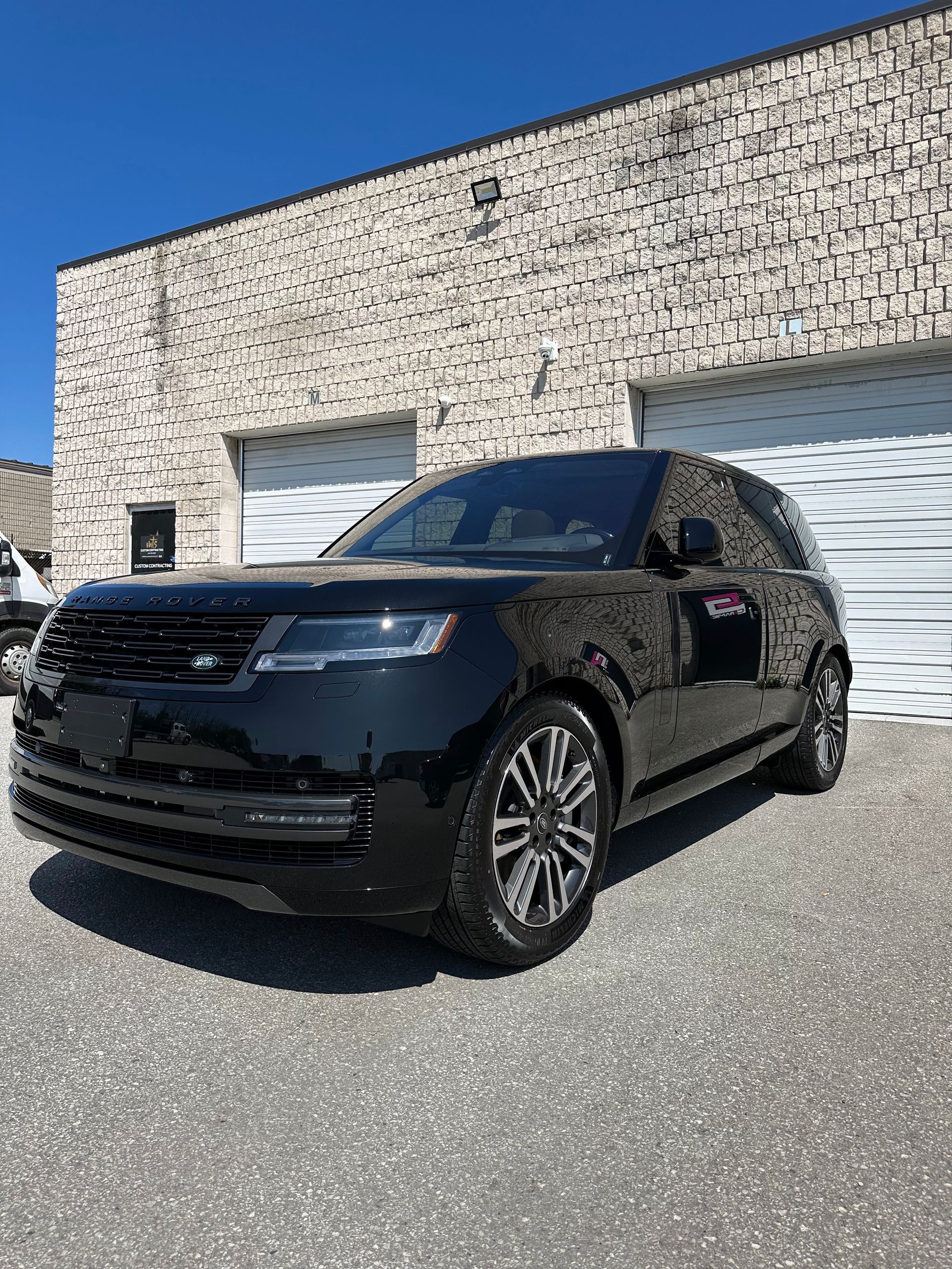 A black Land Rover SUV parked on a gravel lot in front of a white stone building with two garage doors under a clear sky.