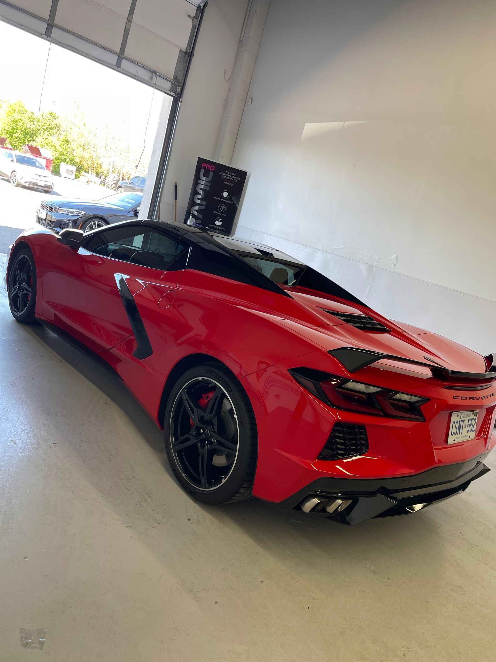 A red Chevrolet Corvette parked inside a brightly lit garage, shown from a rear three-quarter angle.