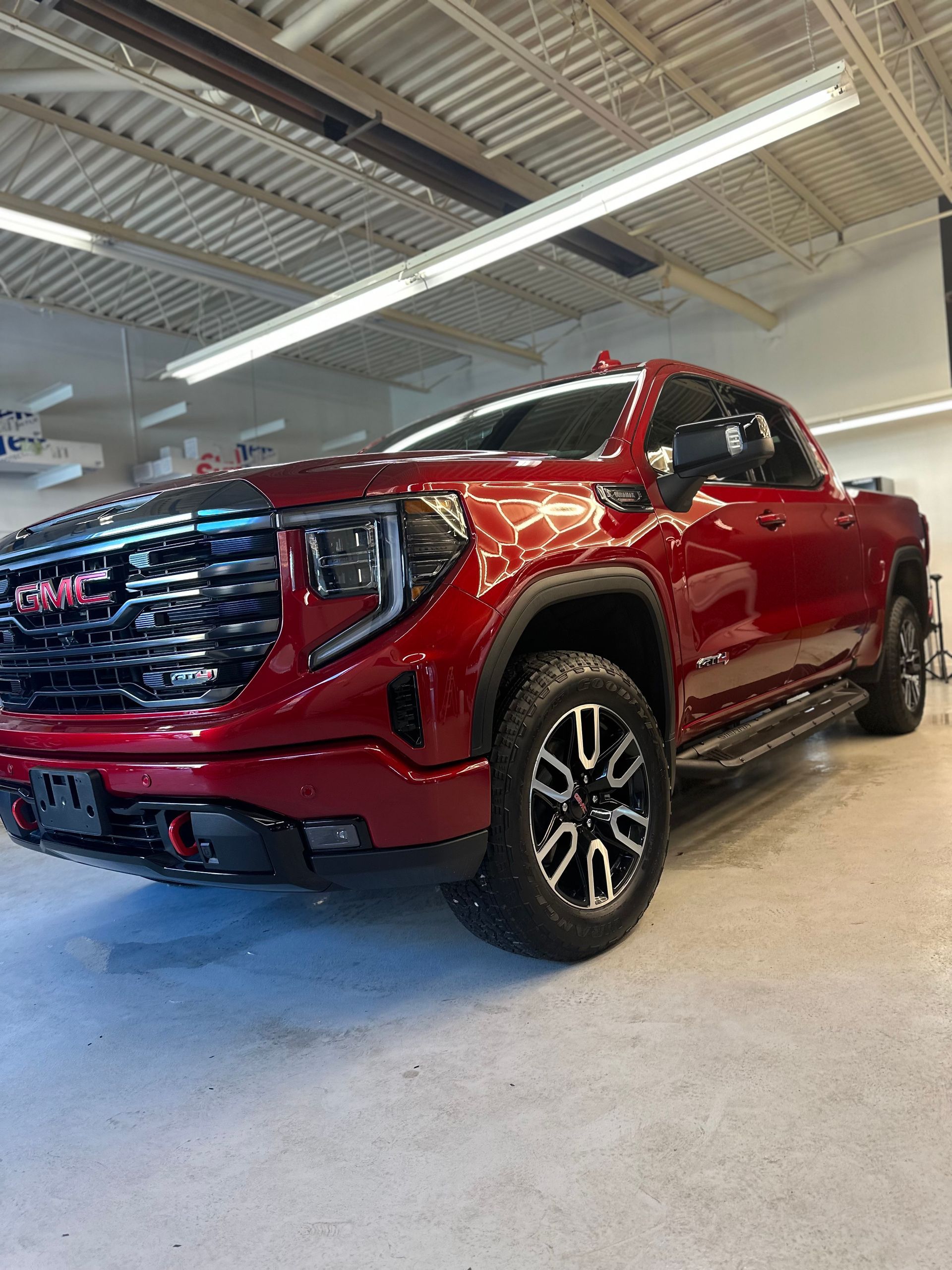 A metallic red GMC Sierra pickup truck parked inside a bright, industrial garage with a concrete floor.