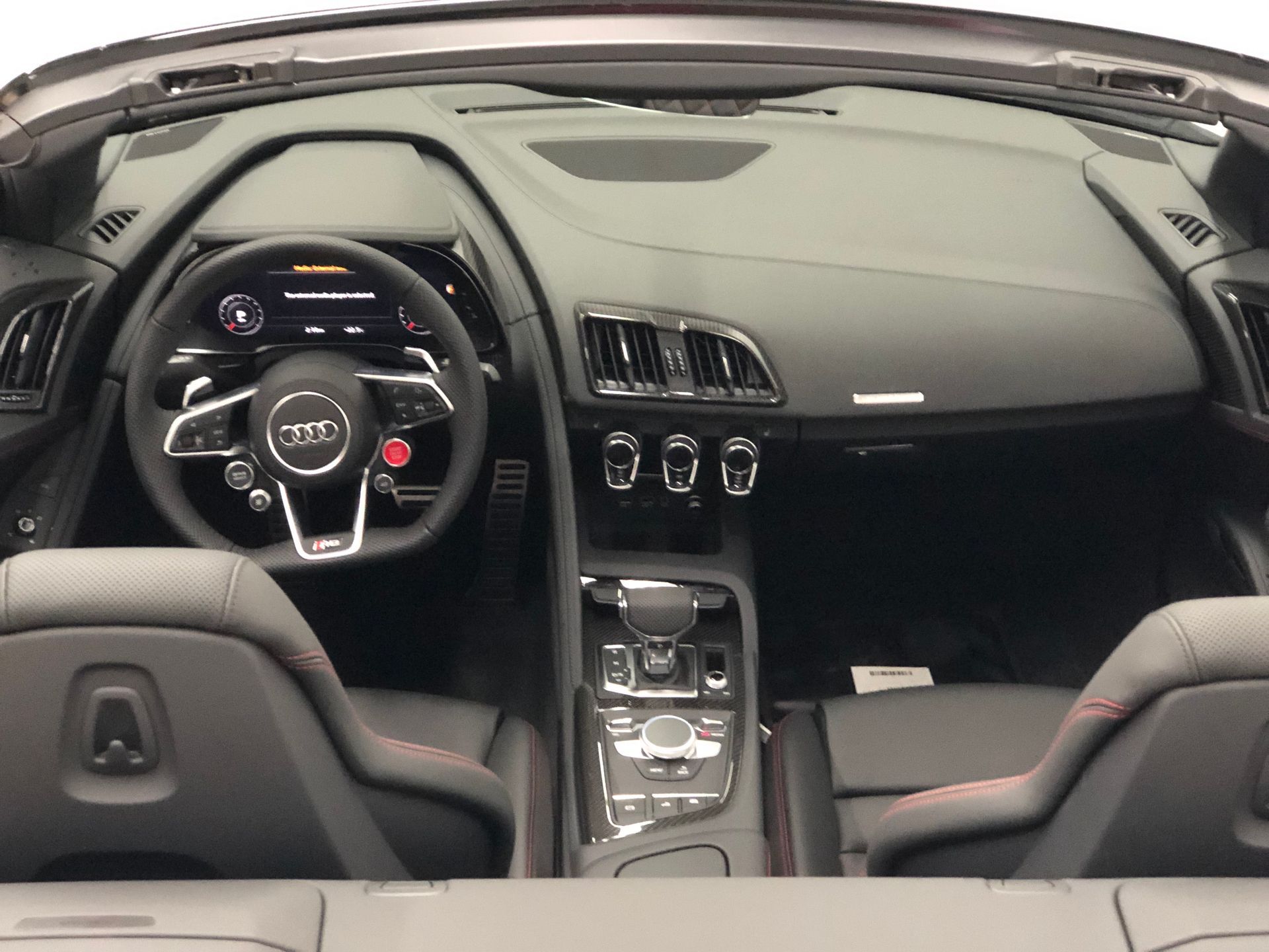 The interior of an Audi R8 convertible, showing the steering wheel, digital dashboard, and center console.
