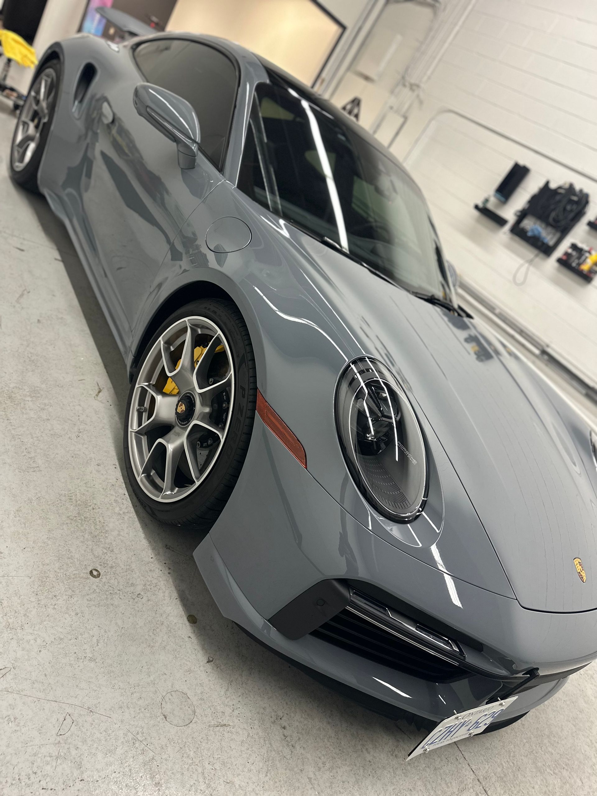 A gray Porsche sports car parked inside a well-lit, industrial garage or detailing shop.