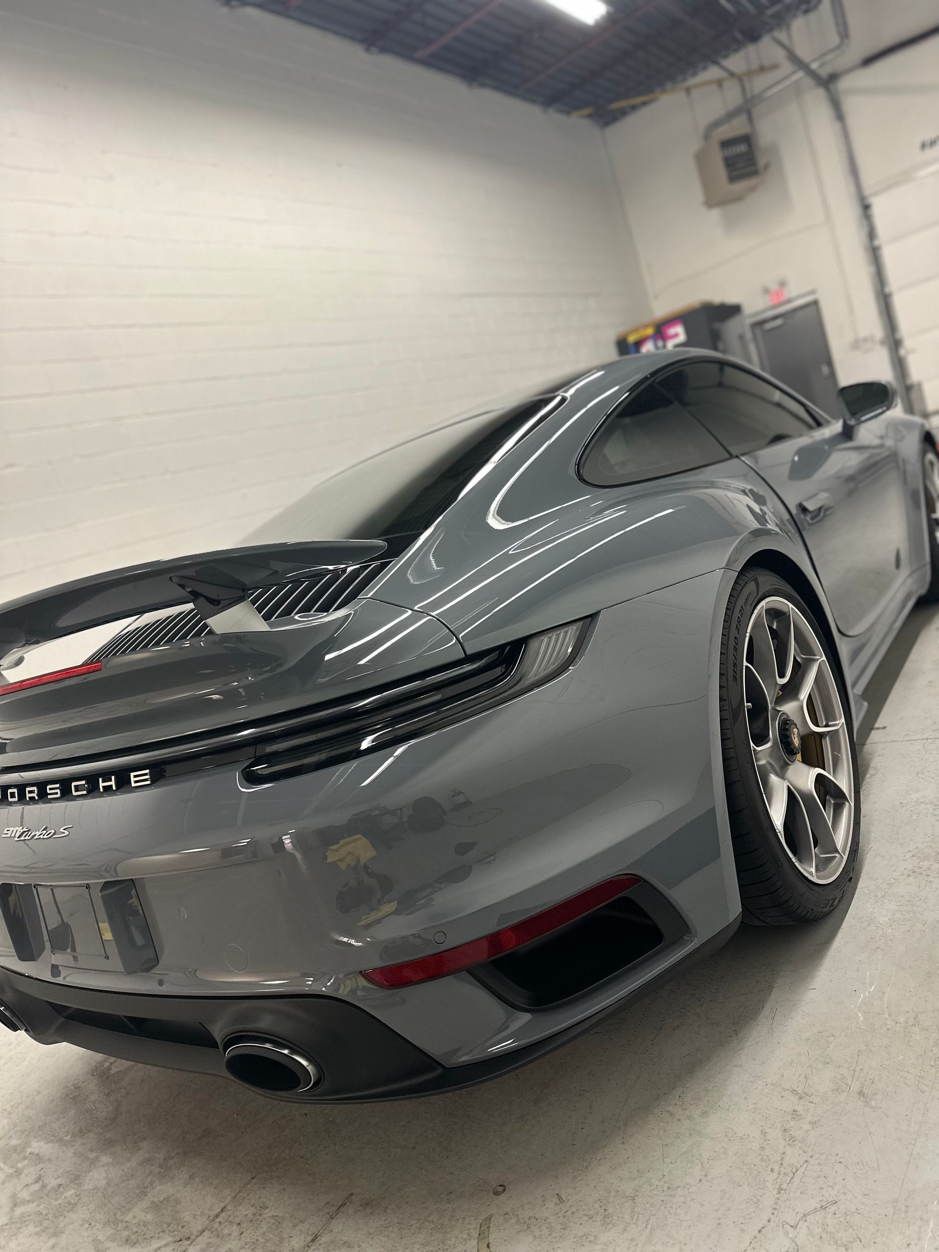 A sleek, grey Porsche 911 parked inside a brightly lit, industrial-style garage.