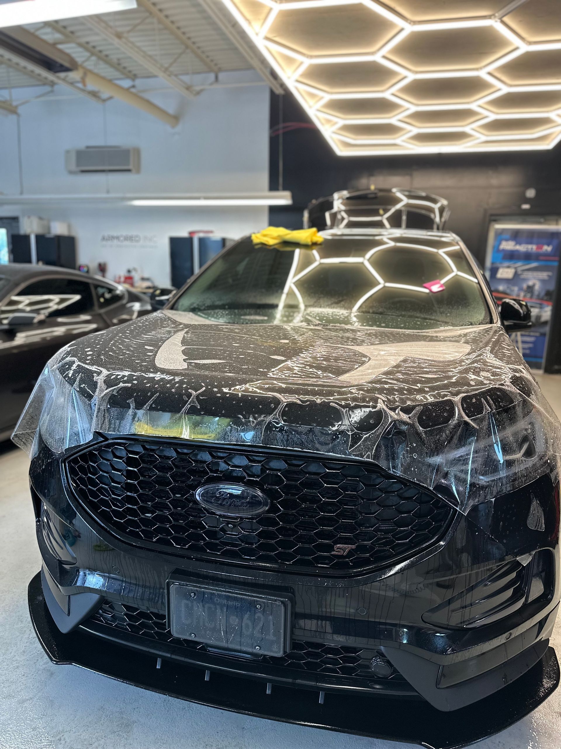 A black SUV in a garage under hexagonal lights, covered in soapy water for a detailing service.