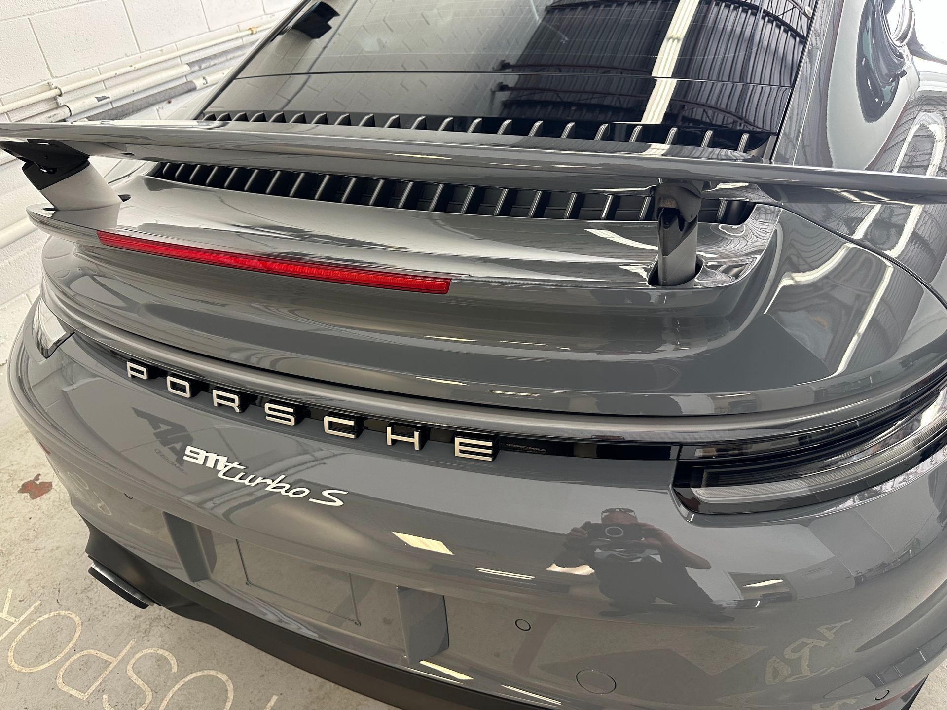 A rear view of a gray Porsche 911 Turbo S featuring a prominent rear spoiler and distinctive taillight bar.