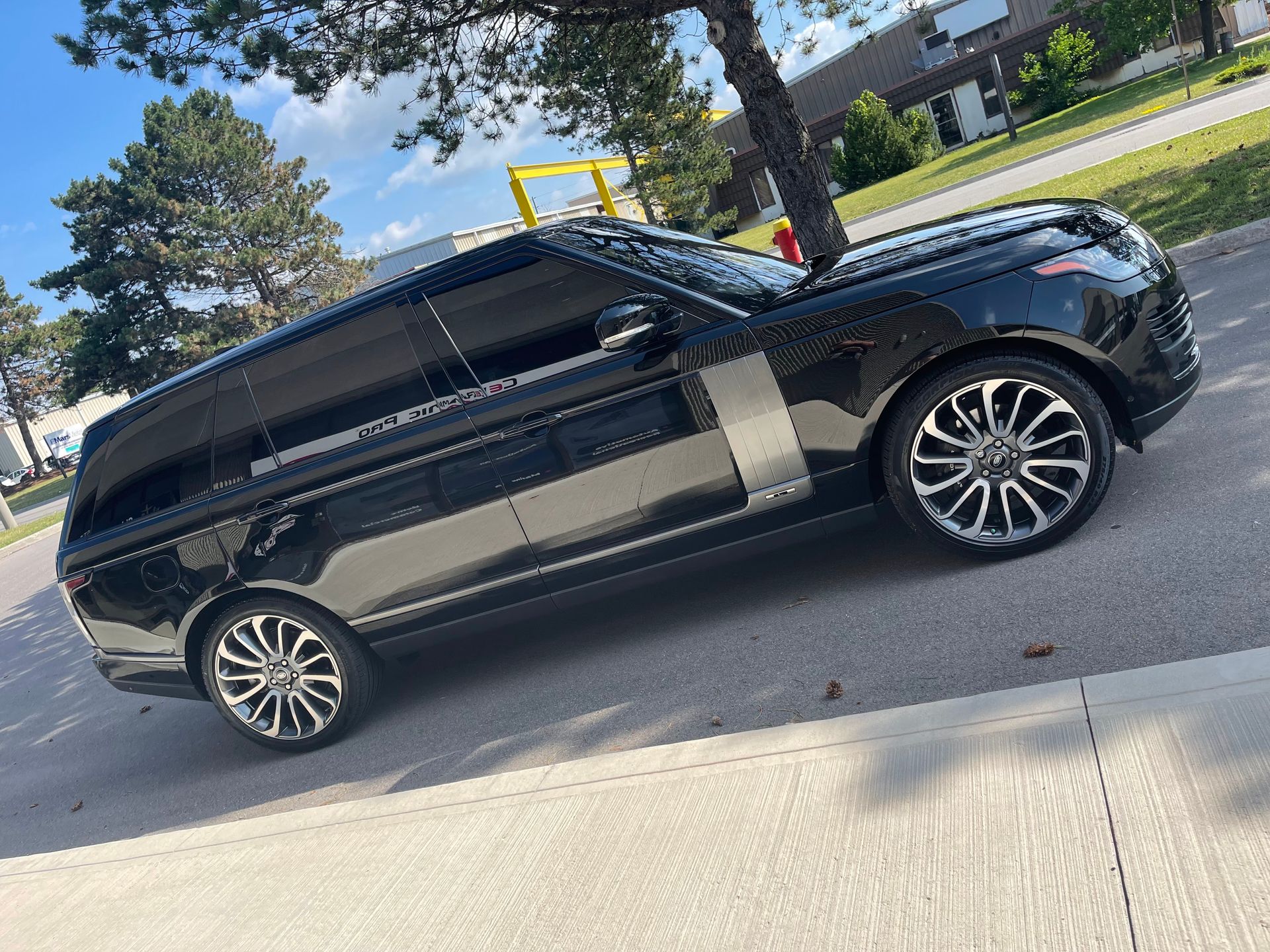 A side profile of a black Range Rover parked on the side of a road near a tree and a grassy area.