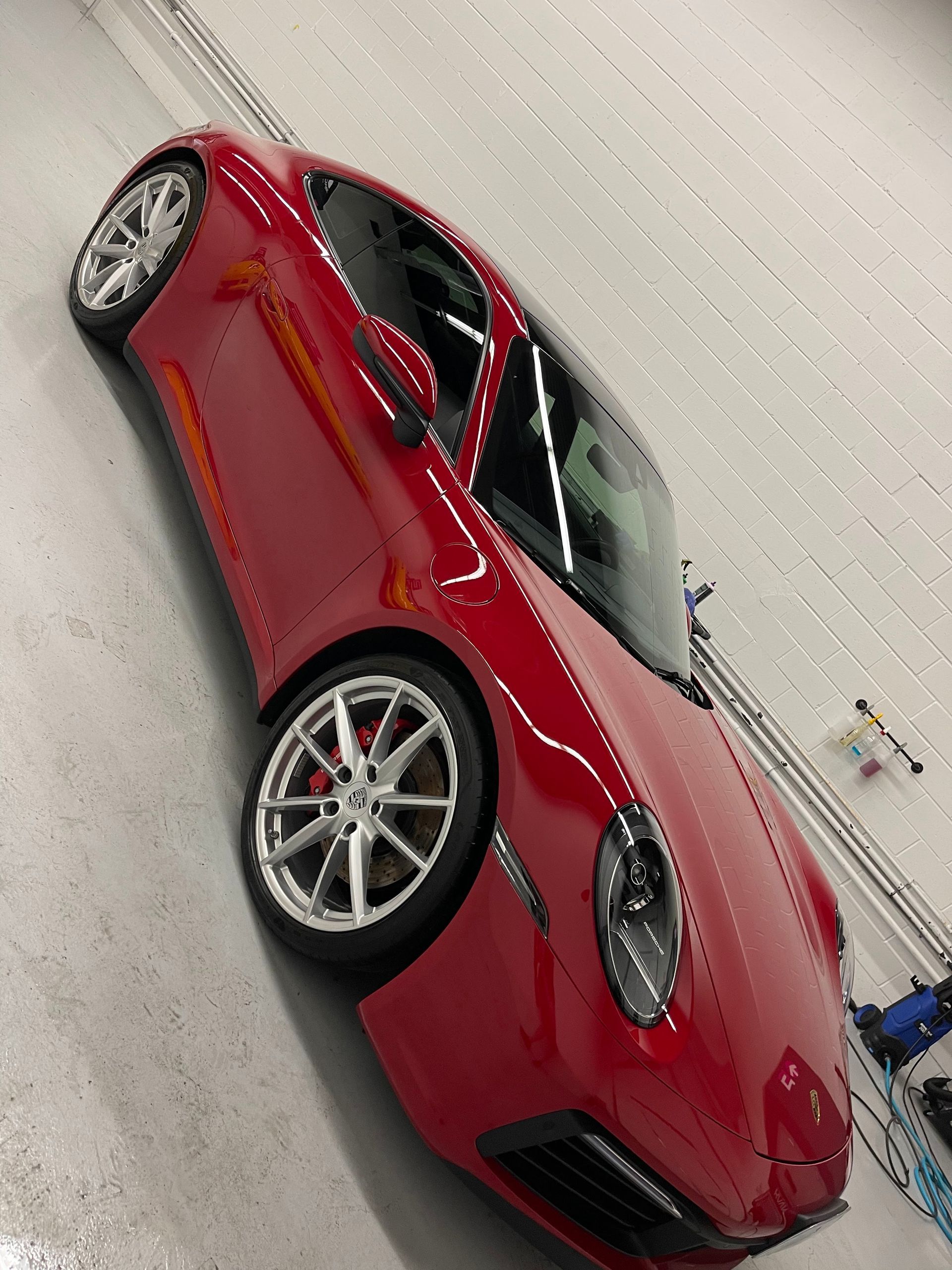 A vibrant red Porsche sports car parked inside a bright, clean garage with white tiled walls.