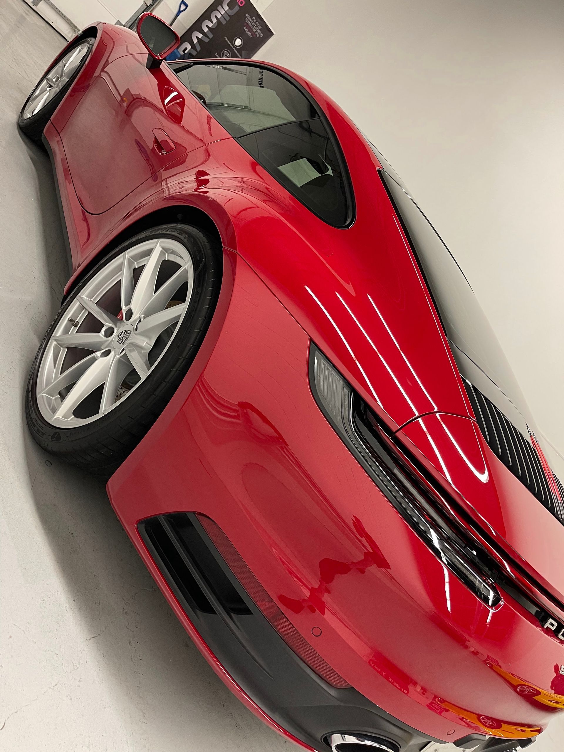 A glossy red Porsche sports car parked at a slight angle in a clean, bright indoor garage setting.