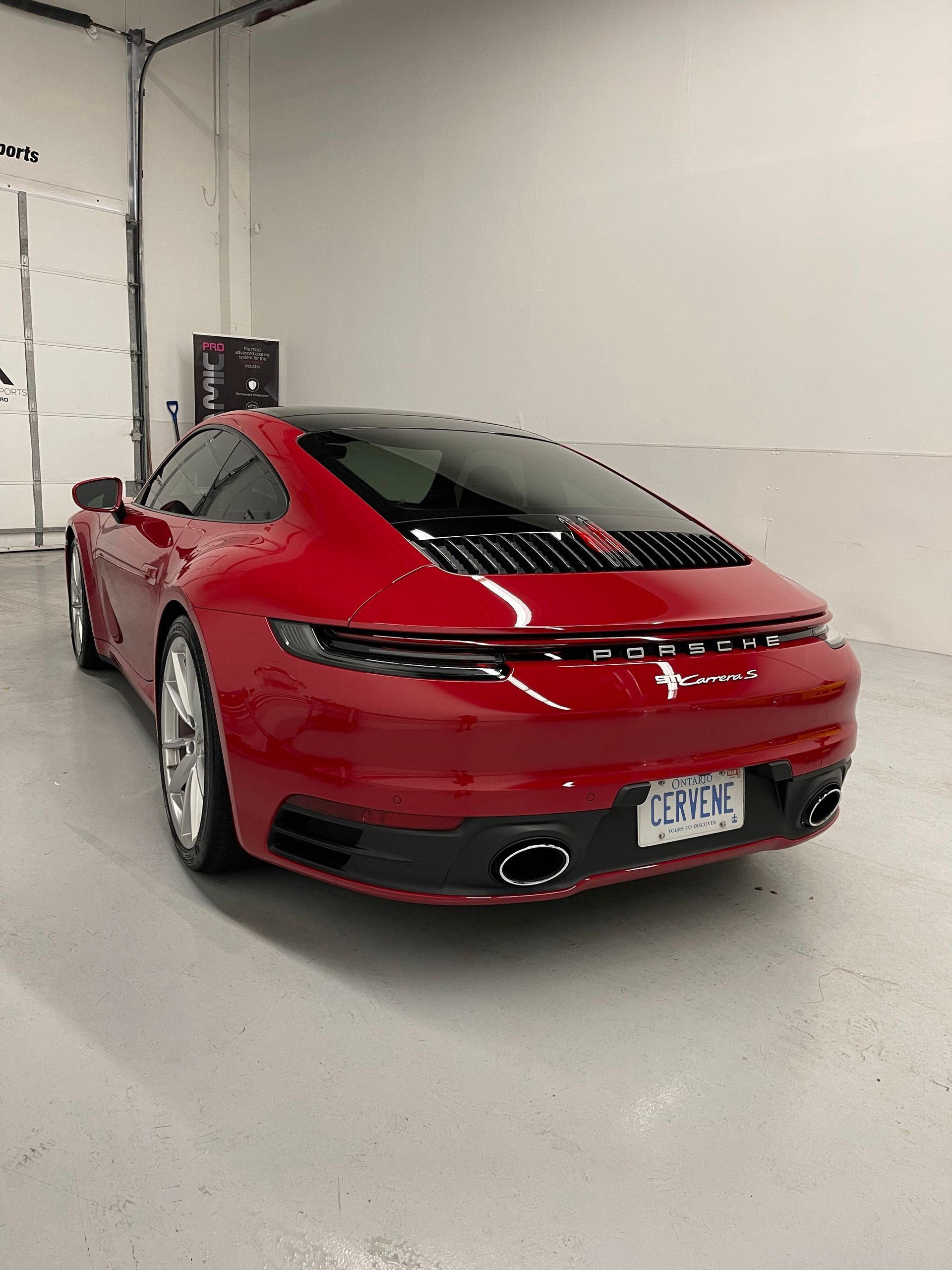 A red Porsche 911 parked inside a garage, showing its sleek rear profile and dual exhaust pipes.