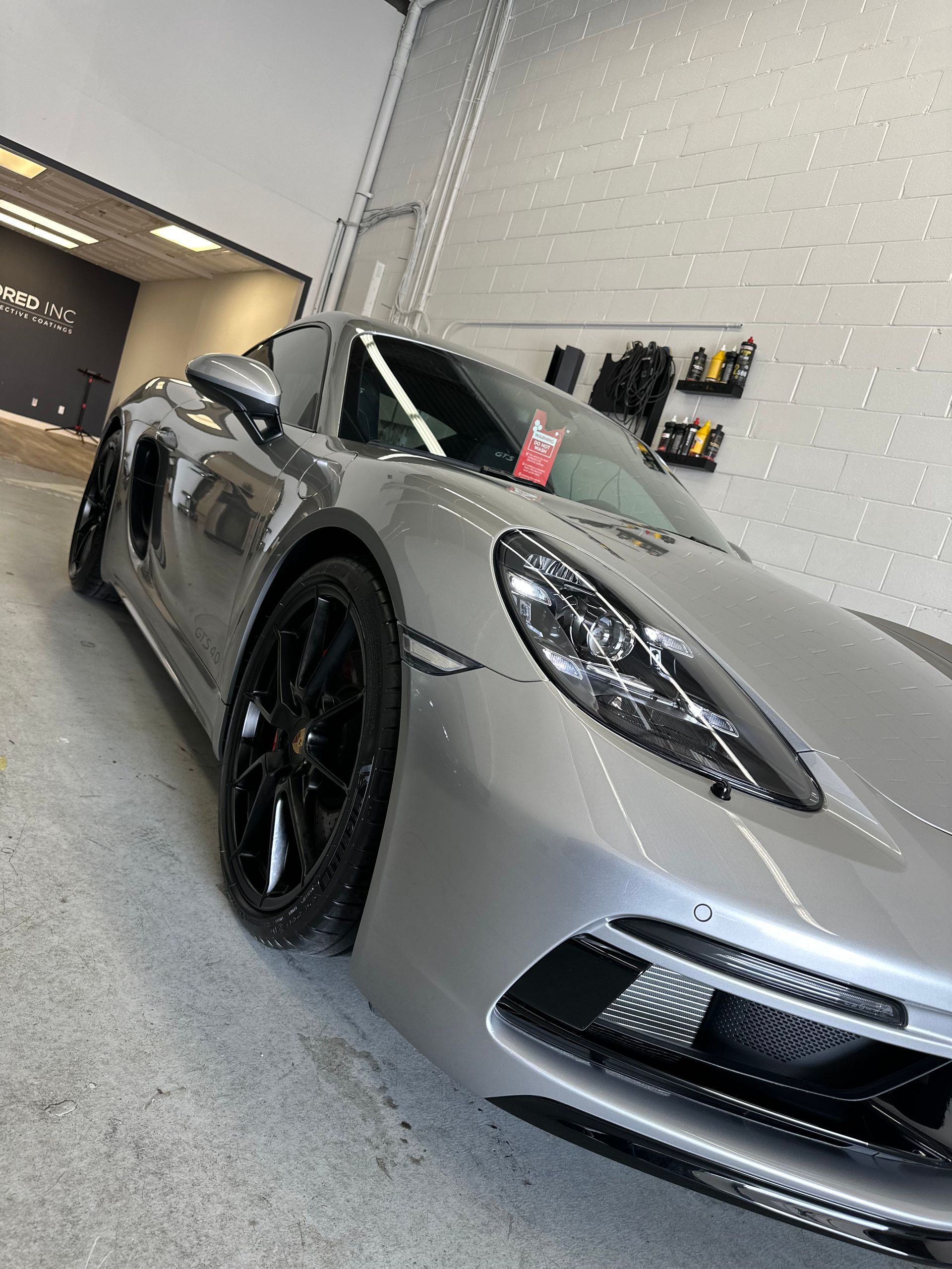 A silver Porsche sports car parked inside a clean, well-lit garage with black wheels and a red interior accent visible.