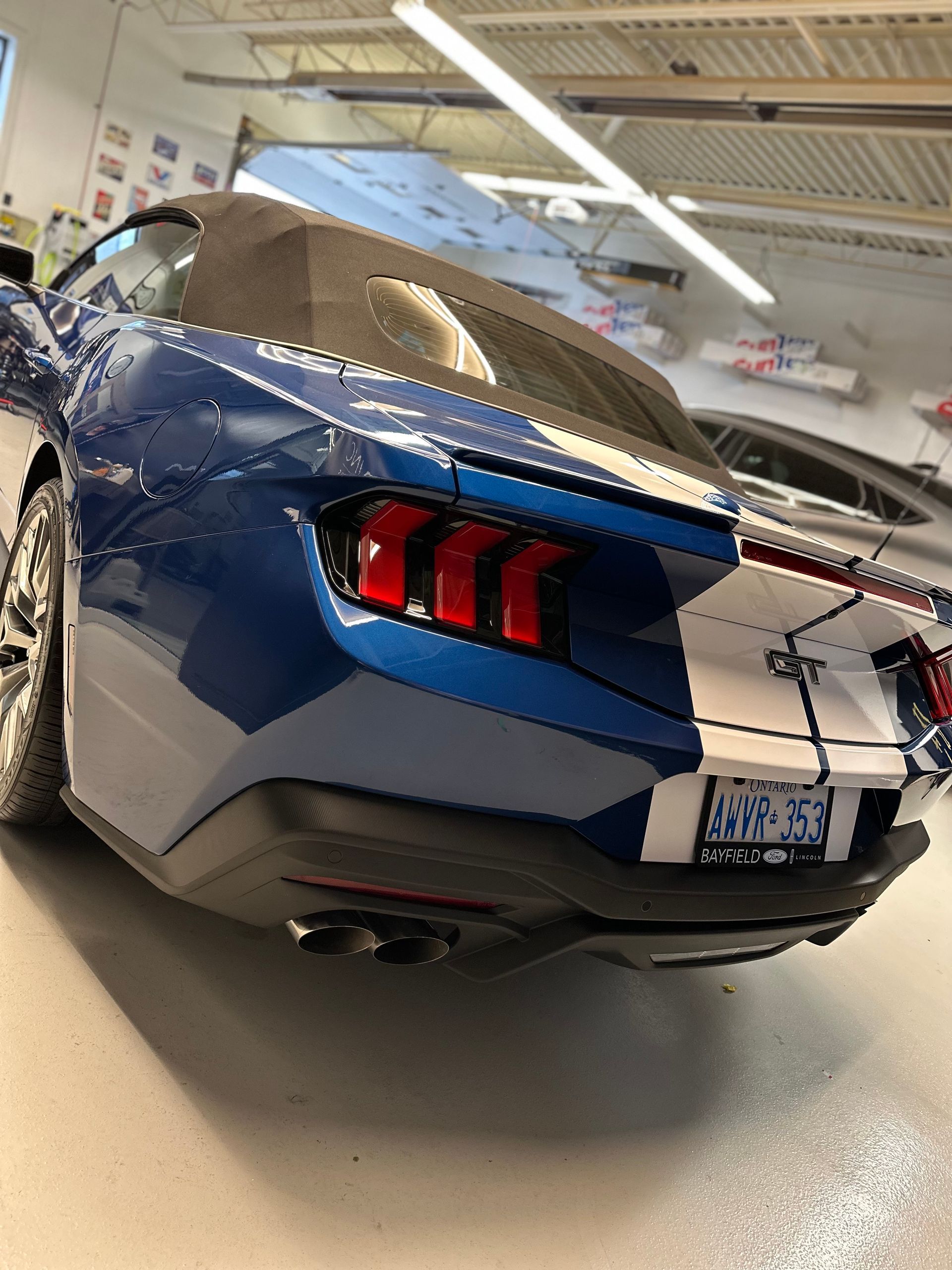A blue Ford Mustang GT convertible with a white racing stripe parked inside a garage.
