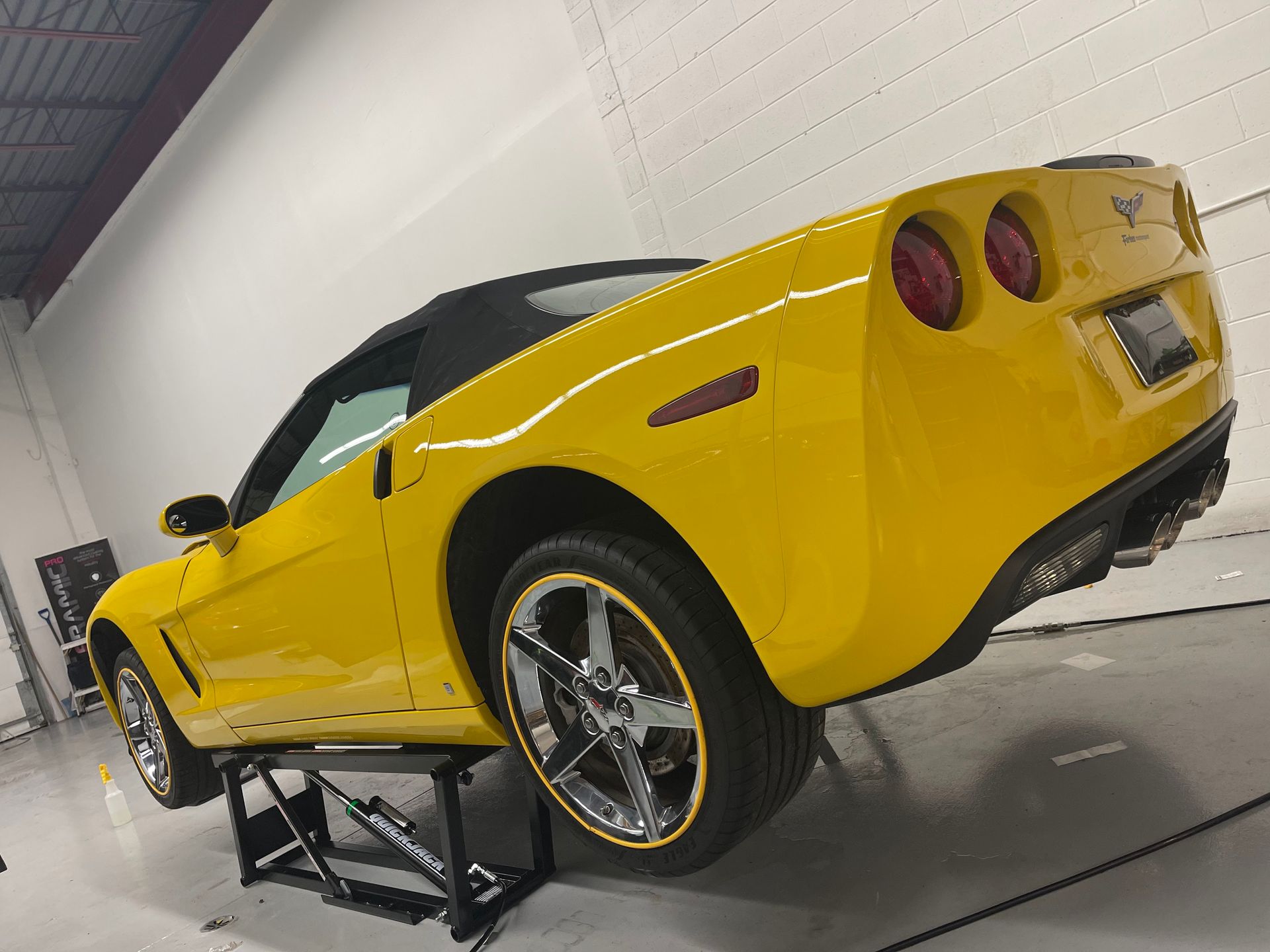 A bright yellow Chevrolet Corvette convertible is elevated on a lift inside a professional garage.