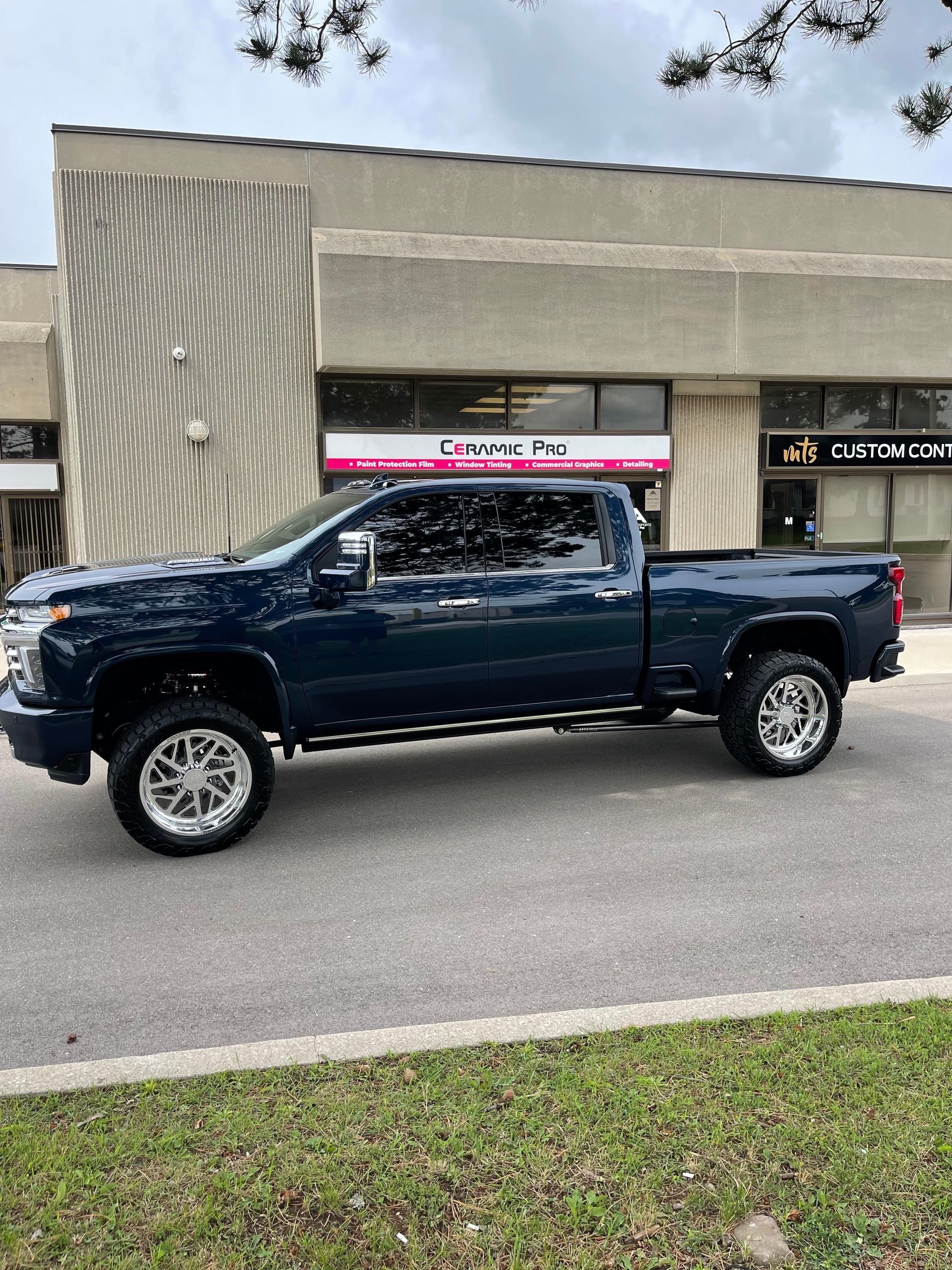 A dark blue crew cab pickup truck parked in front of a commercial building with large glass windows.