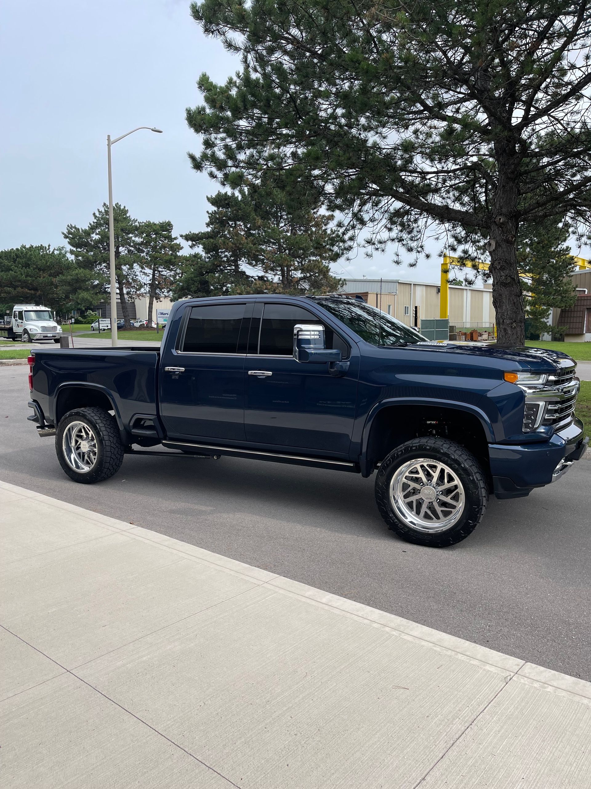 A dark blue lifted crew cab pickup truck parked on the side of a road near a tree and a utility pole.
