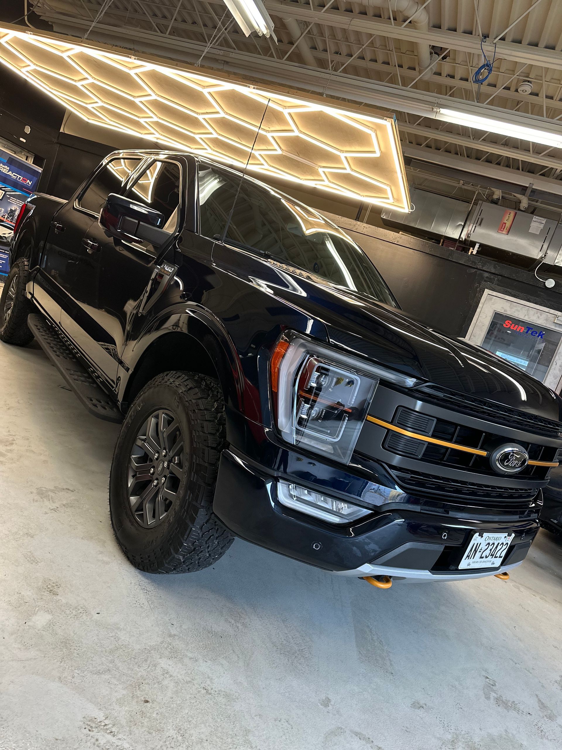 A black Ford F-150 pickup truck parked inside a bright, modern showroom with hexagonal ceiling lights.