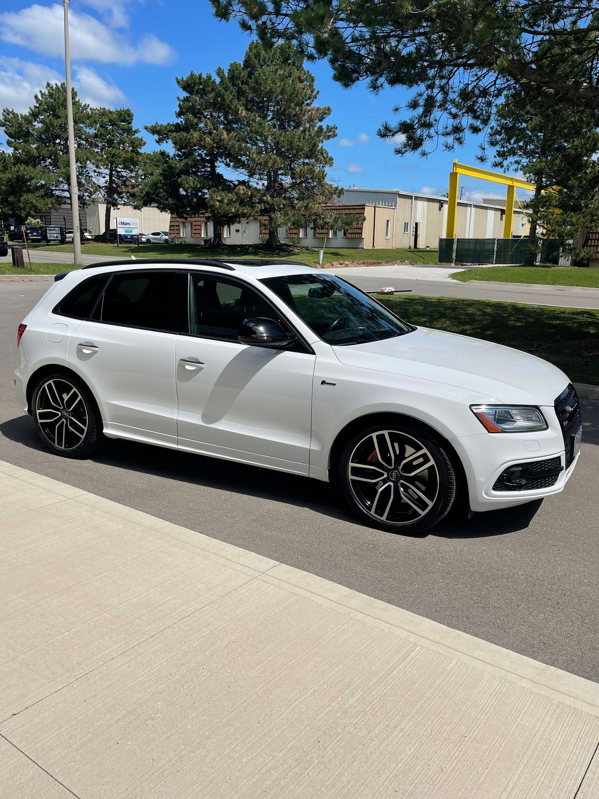 A white Audi SUV parked on an asphalt lot with trees and a building in the background.