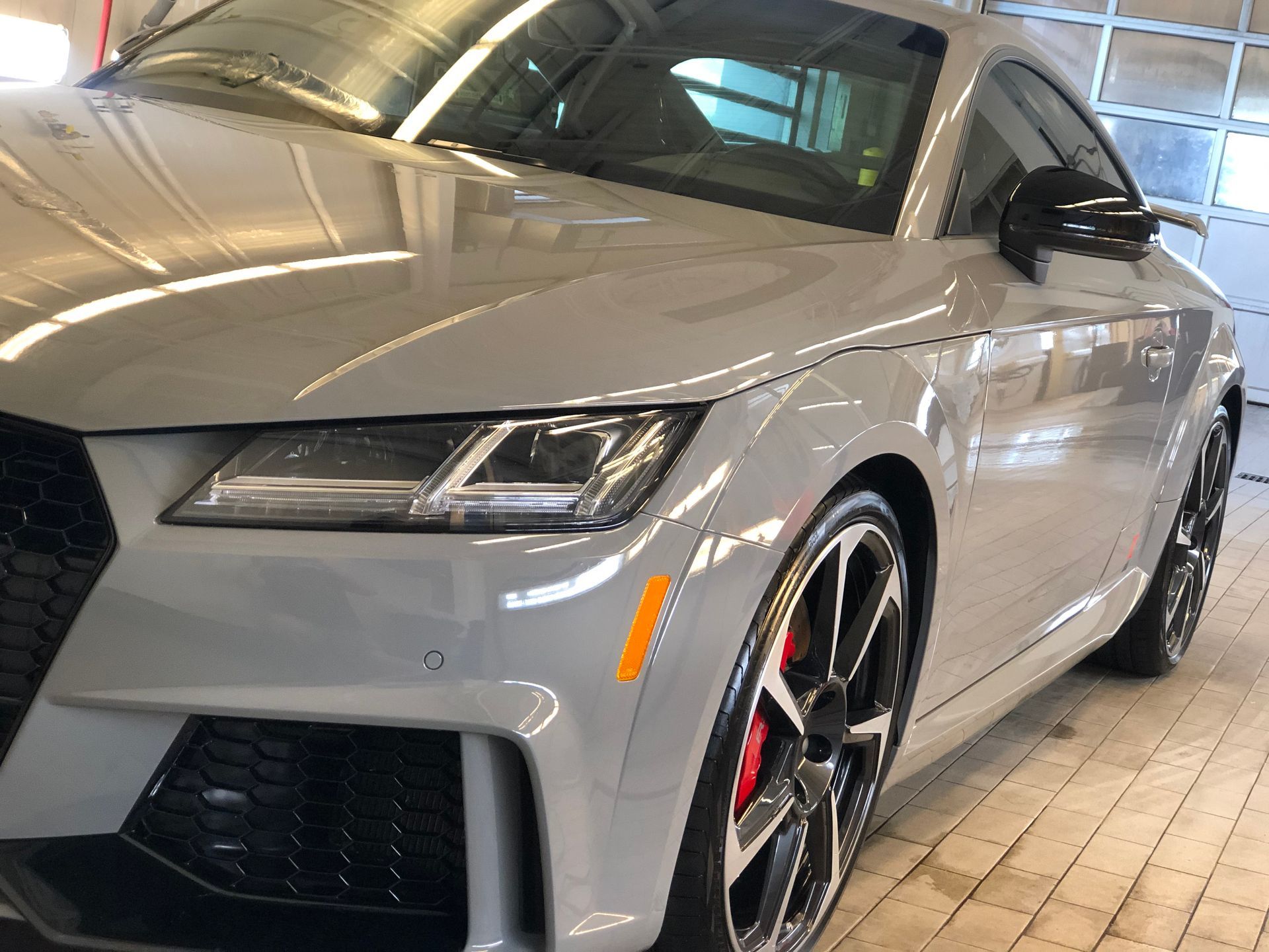 A grey Audi TT RS coupe parked inside a garage, highlighting its sleek design, black wheels, and red brake calipers.