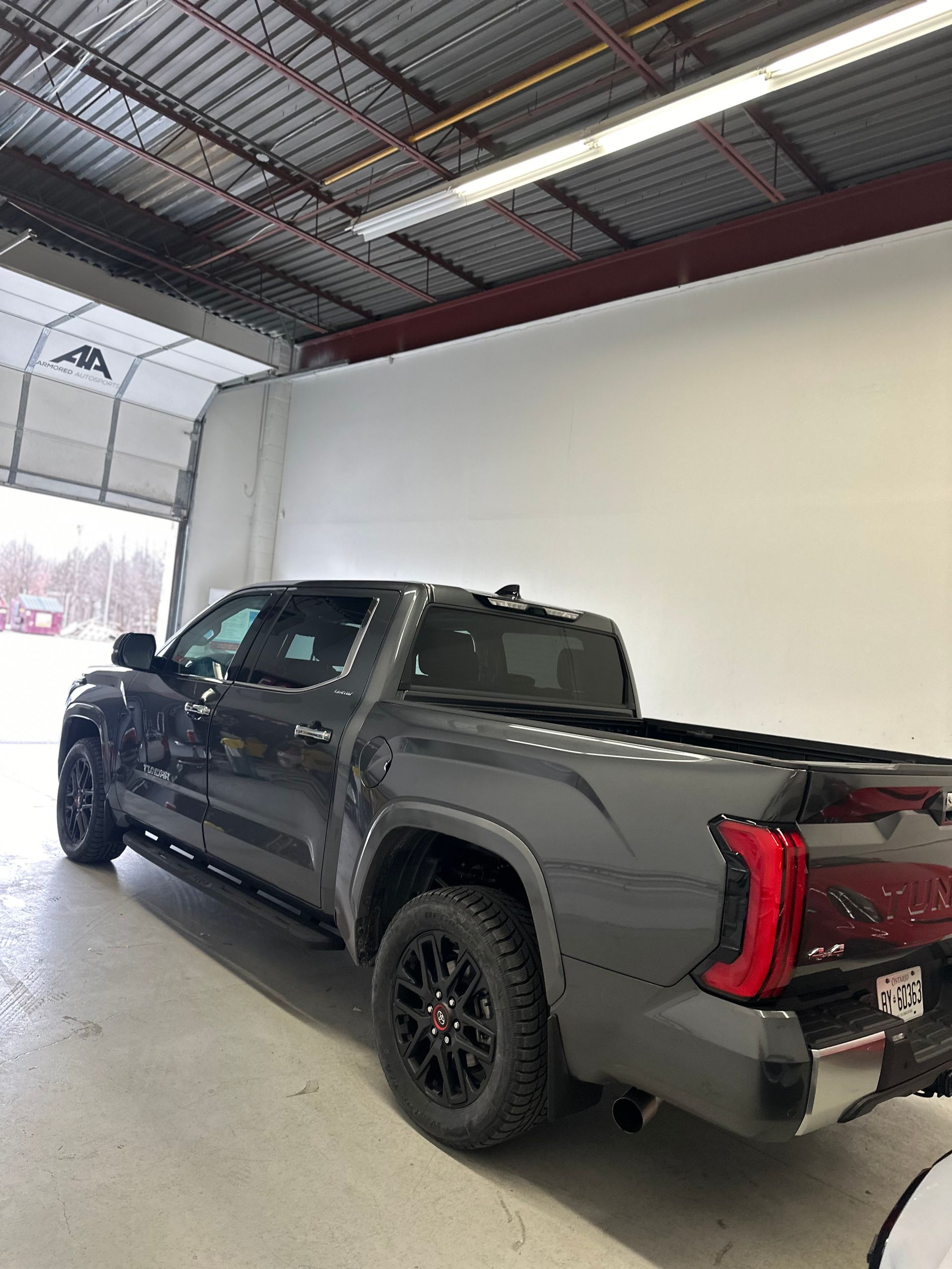 A gray Toyota Tacoma pickup truck parked inside a bright, industrial garage with a large open bay door.