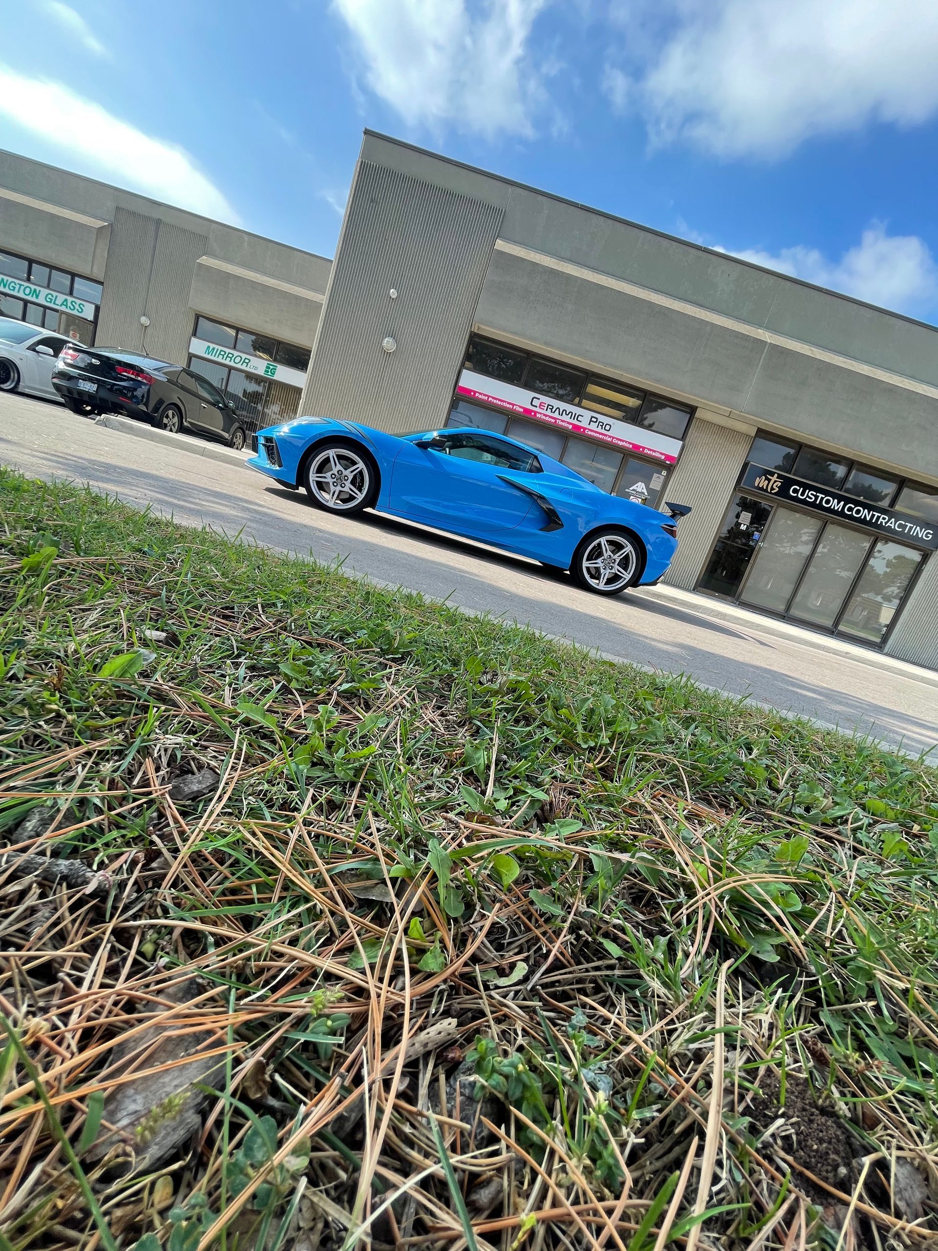 A bright blue sports car parked in front of a modern commercial building on a sunny day.