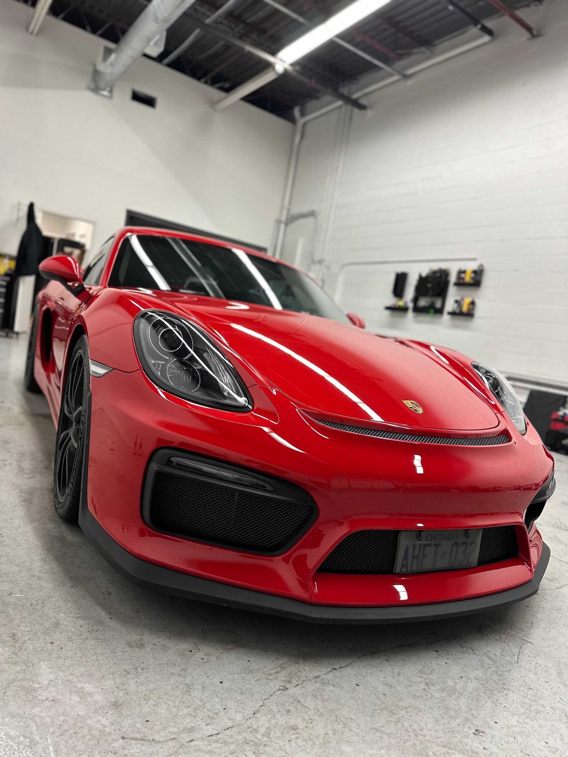 A bright red Porsche sports car parked inside a clean, modern workshop with black wheels and a front air intake.