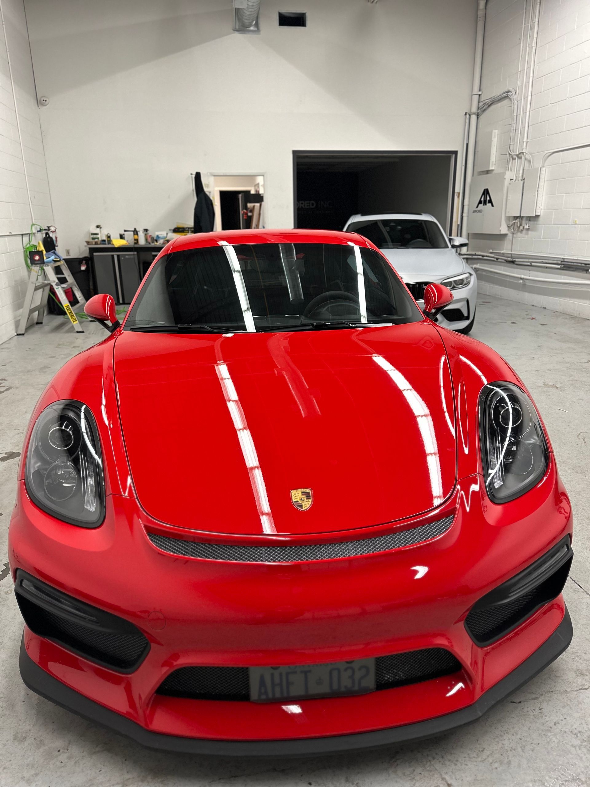 A vibrant red Porsche sports car parked inside a brightly lit automotive workshop, with a second car visible in the back.