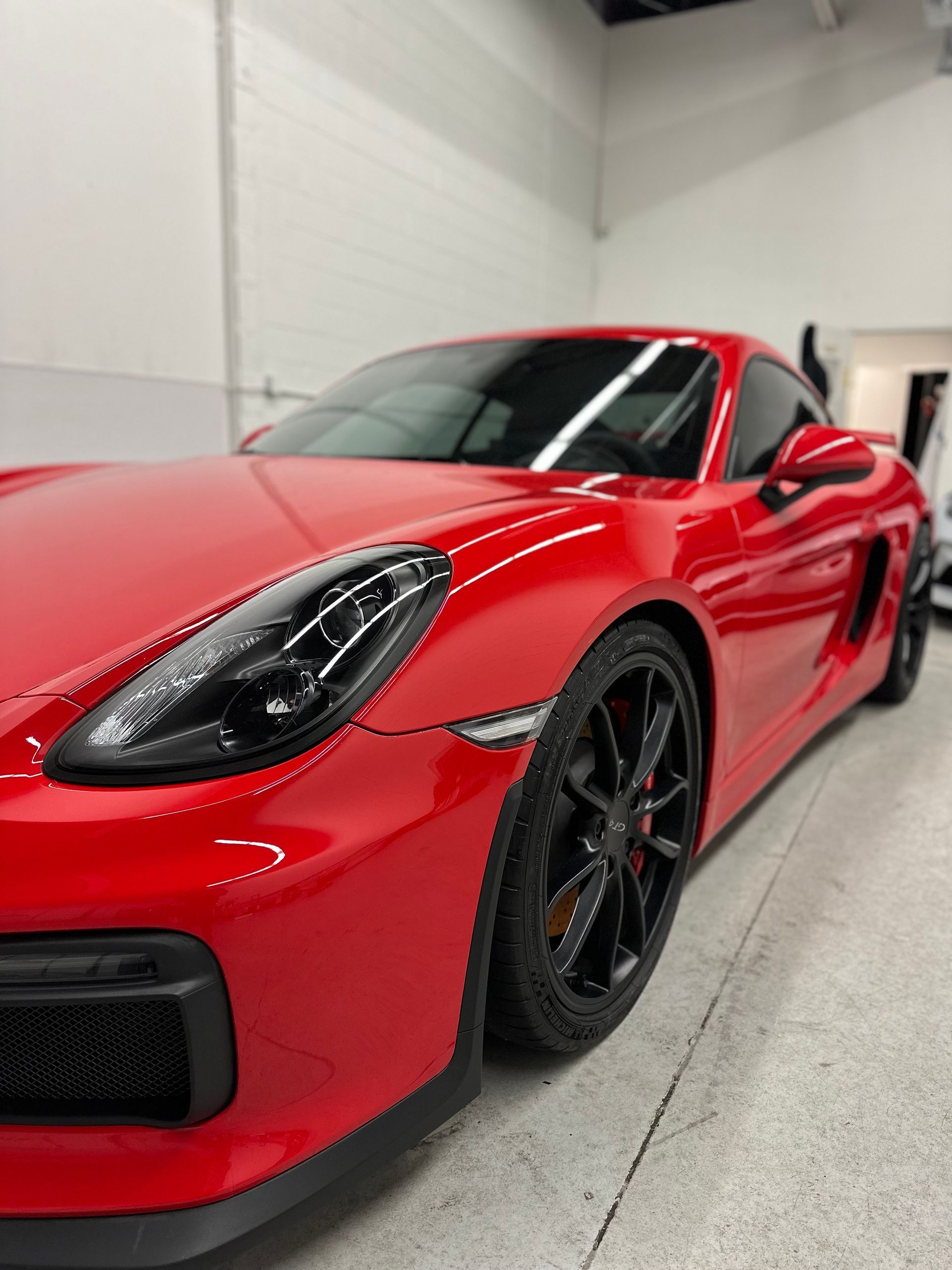 A shiny red Porsche sports car parked inside a bright, clean garage with black rims.