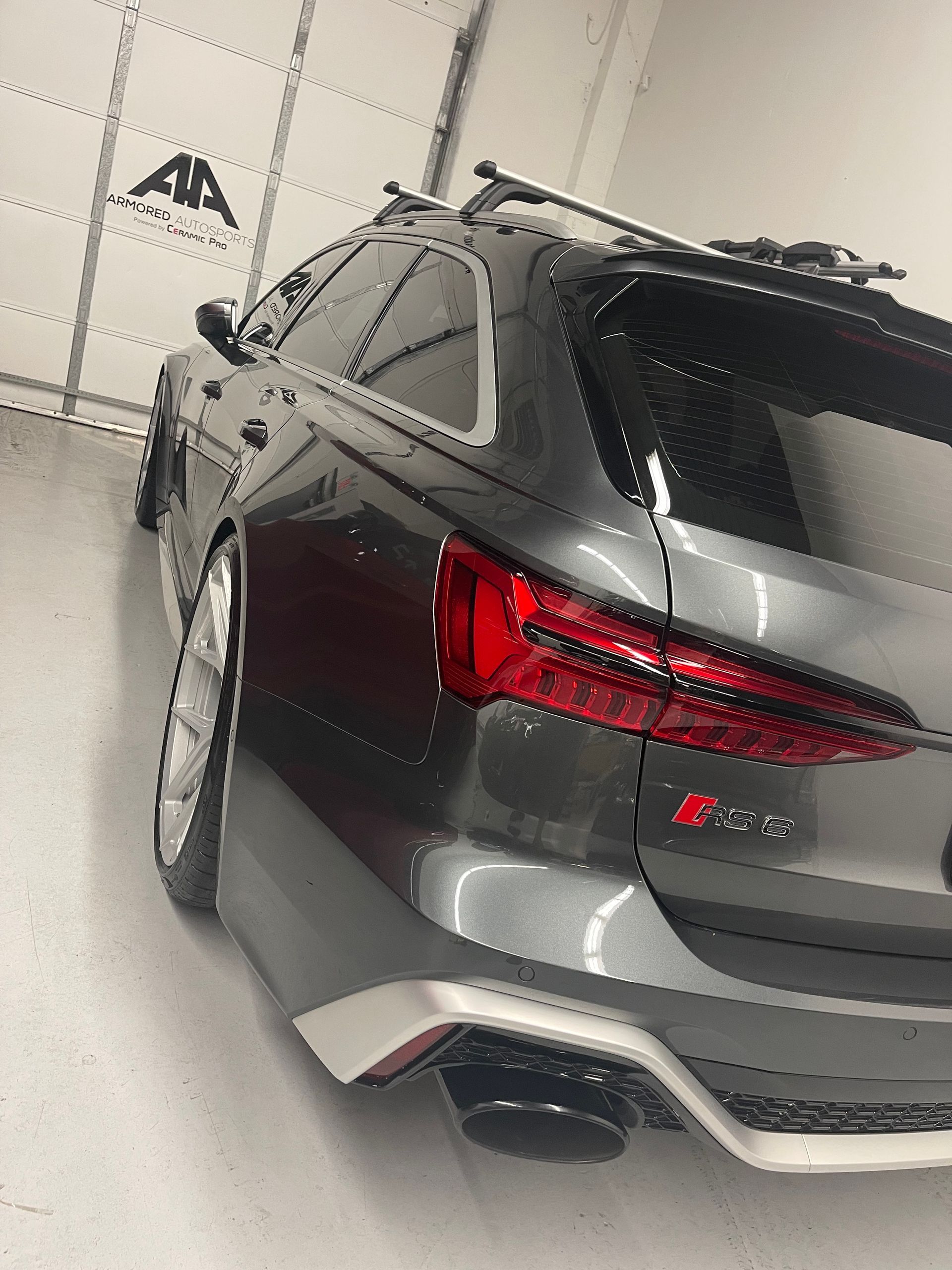 A charcoal gray Audi RS6 Avant wagon parked inside a garage with a roof rack and silver wheels.