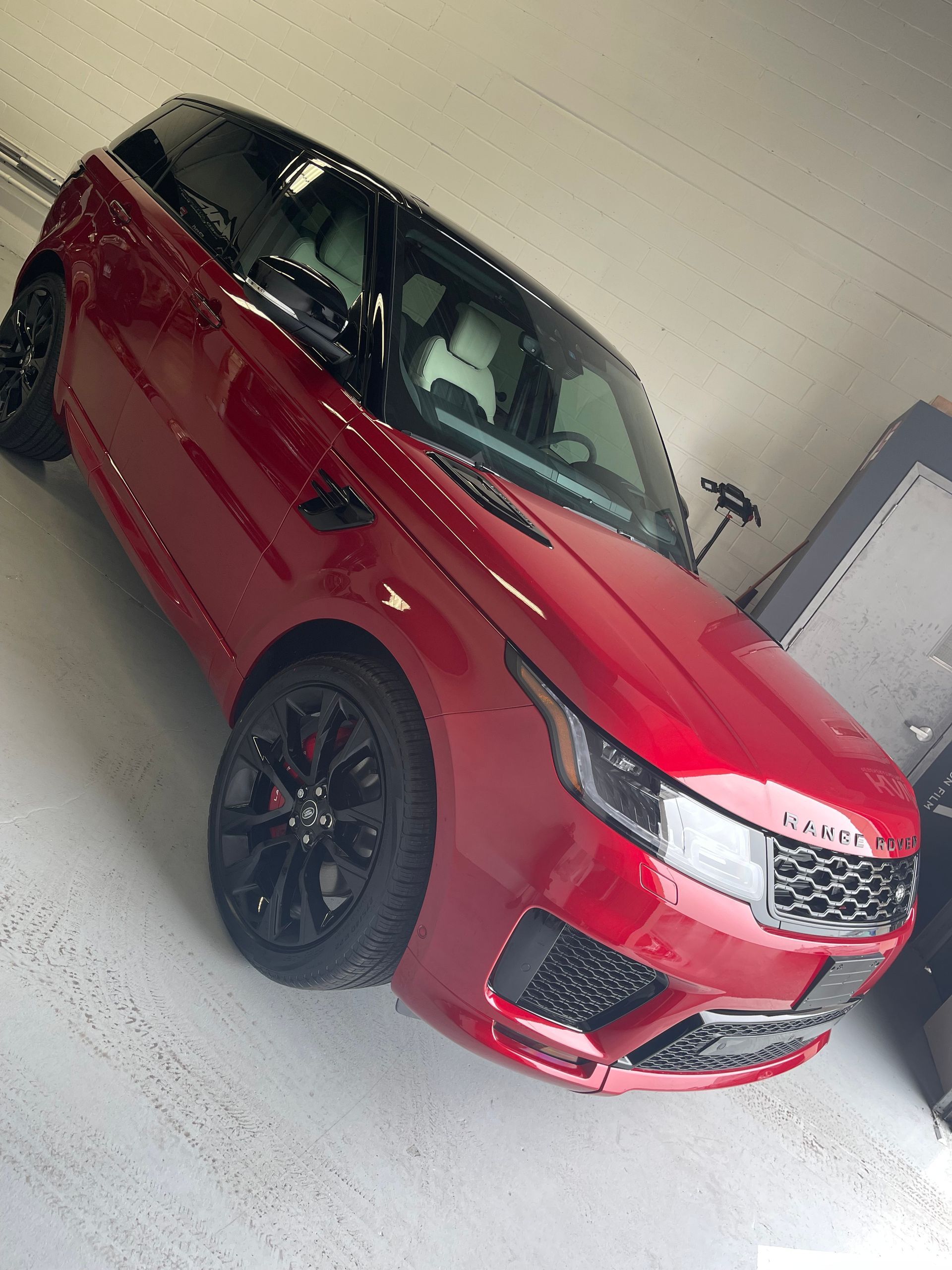 A red Range Rover SUV with black rims and a black roof parked inside a garage.