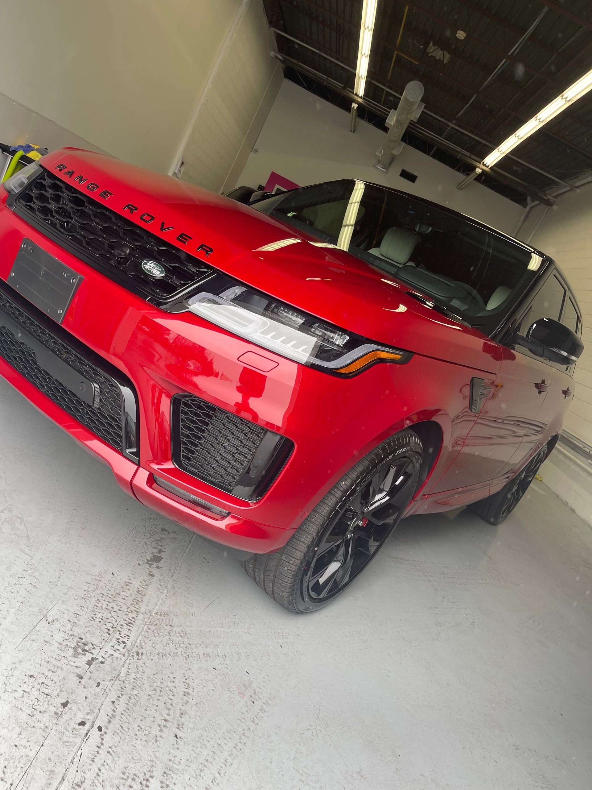 A bright red Range Rover parked at a slight angle inside a brightly lit garage with a white floor.