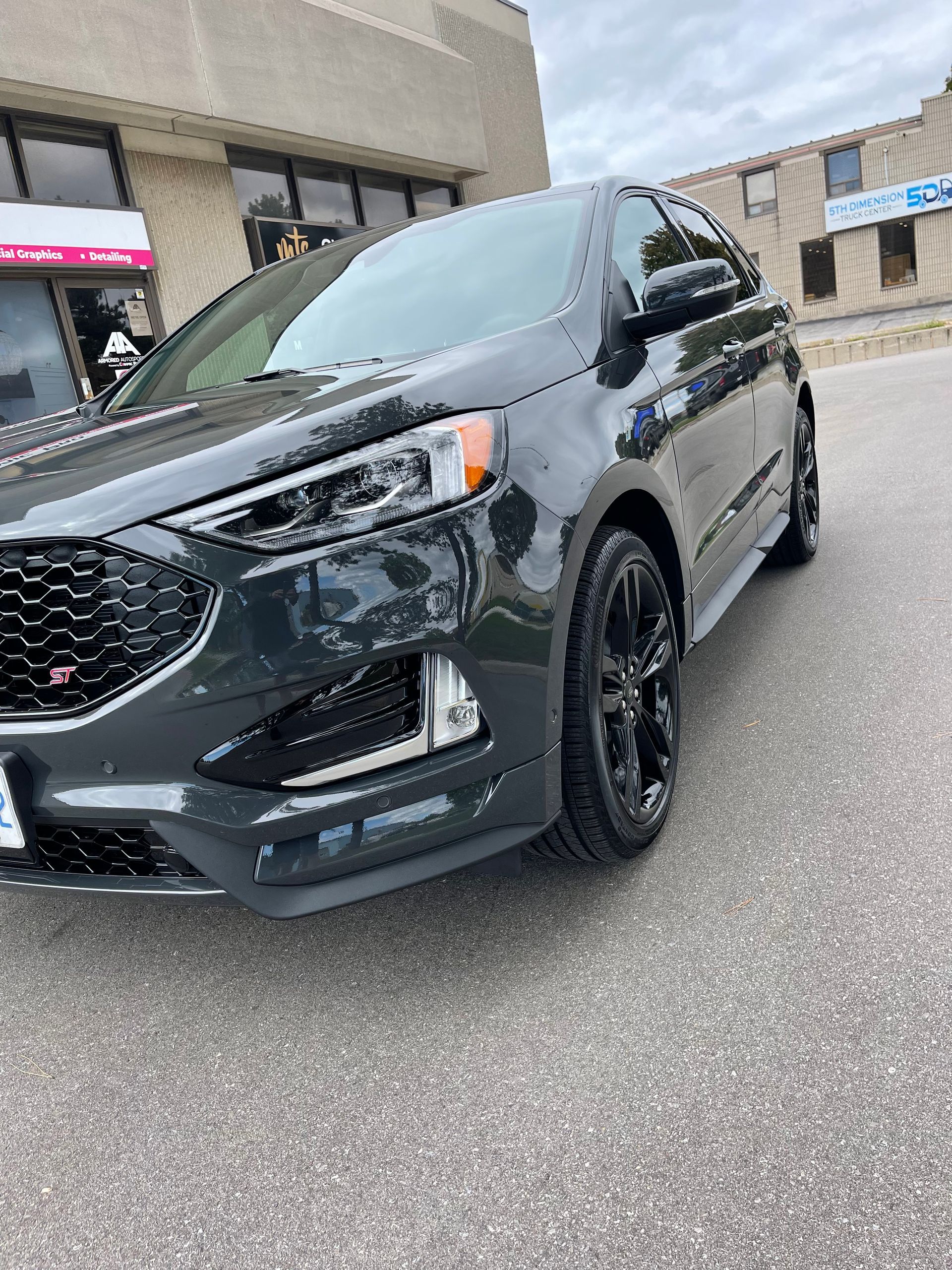 A charcoal gray Ford Edge SUV parked in front of a commercial building on a cloudy day.