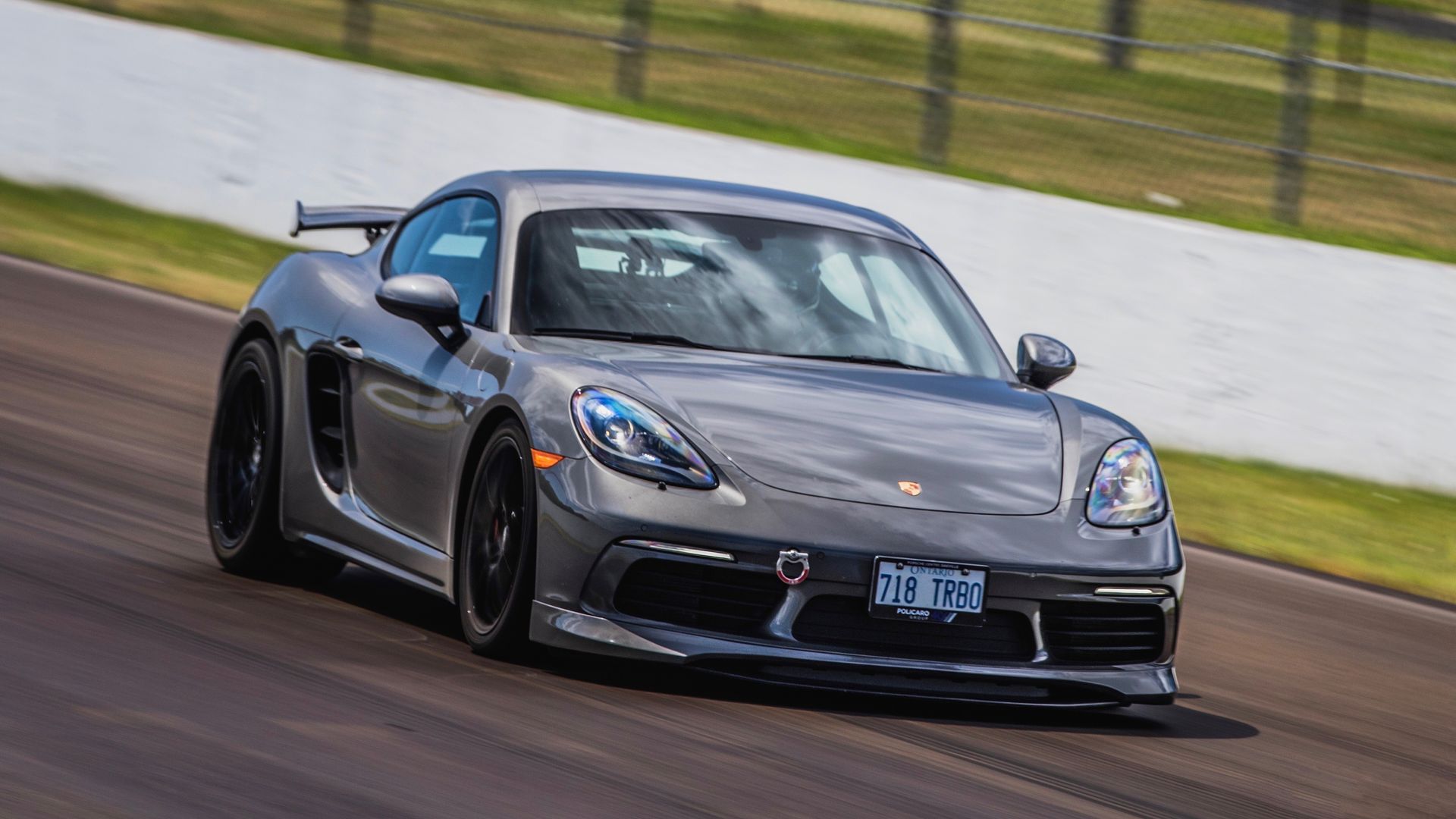 A grey Porsche Cayman driving at speed on a paved racetrack.