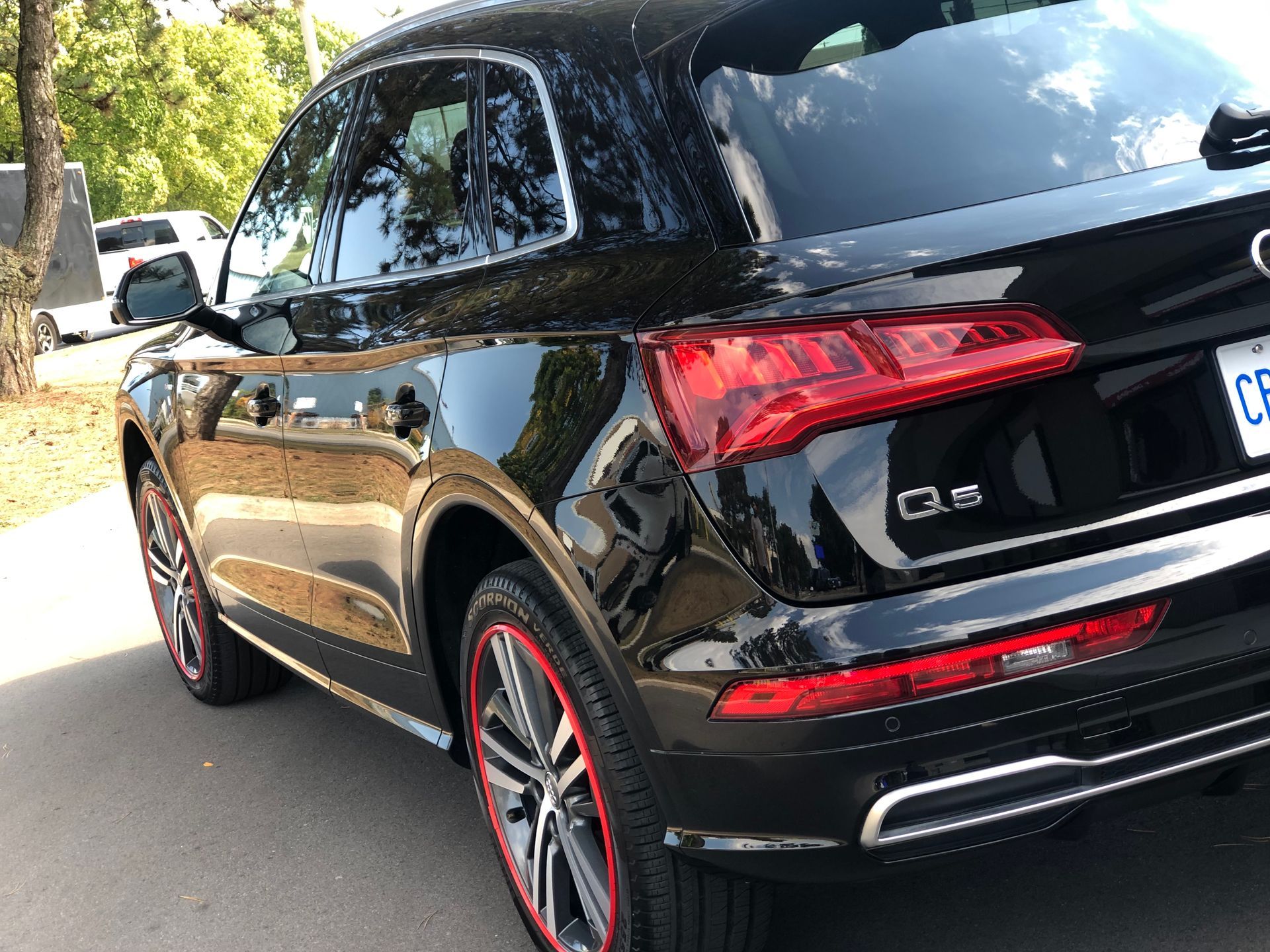 A black Audi Q5 parked outdoors, featuring custom red-rimmed wheels, viewed from a rear-side angle.