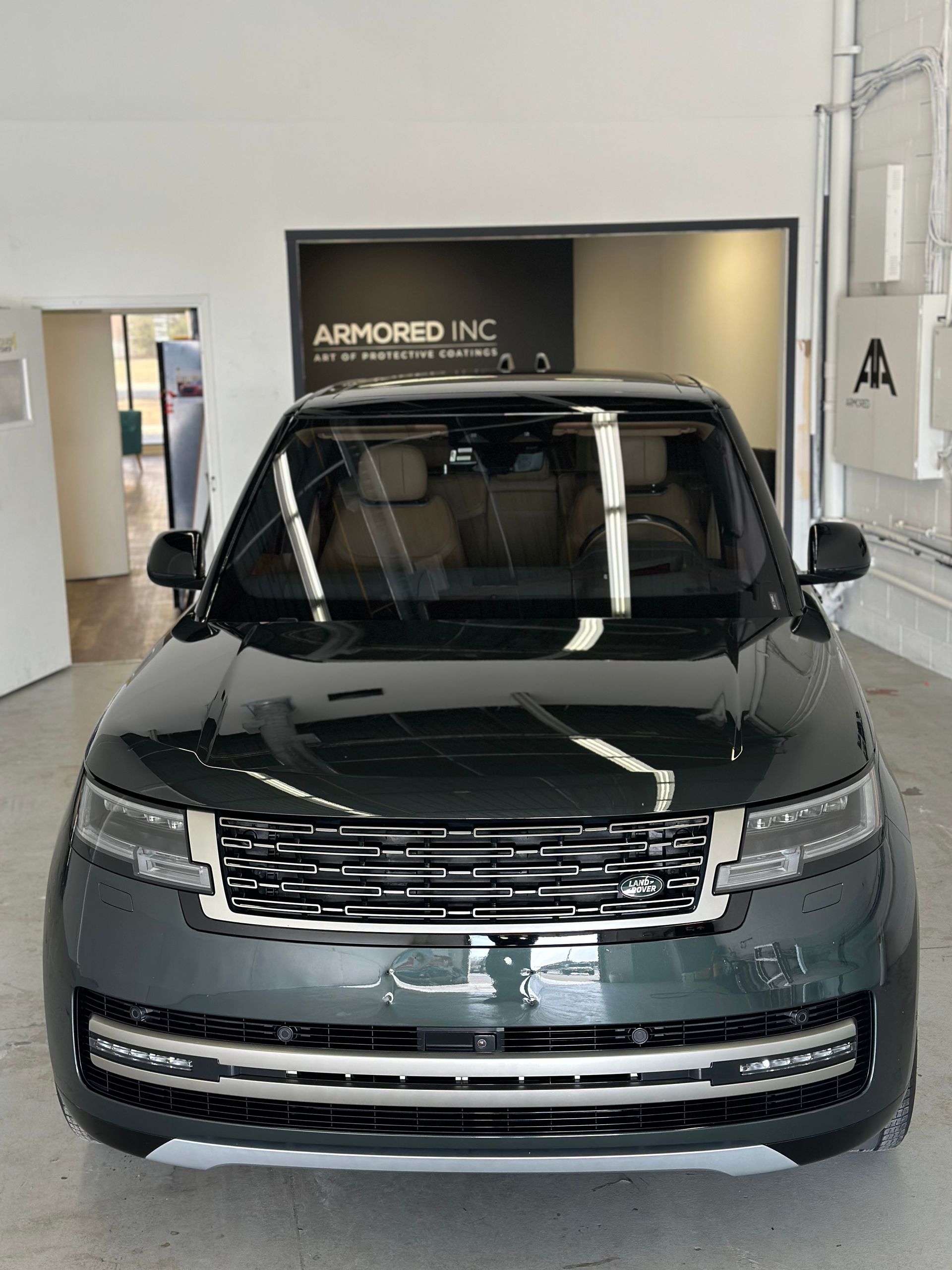 A dark green Range Rover parked inside an Armored Inc. facility, viewed from the front.