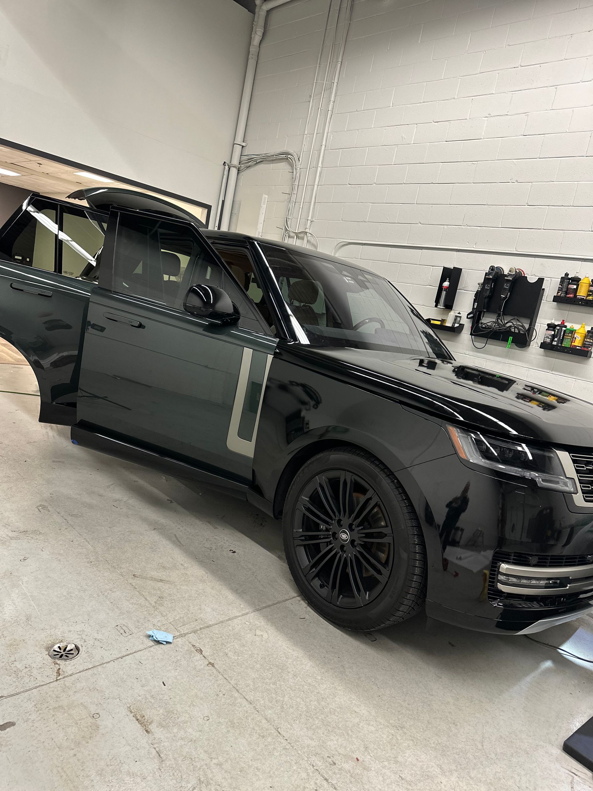 A black Range Rover parked in a workshop with its front and rear doors open.