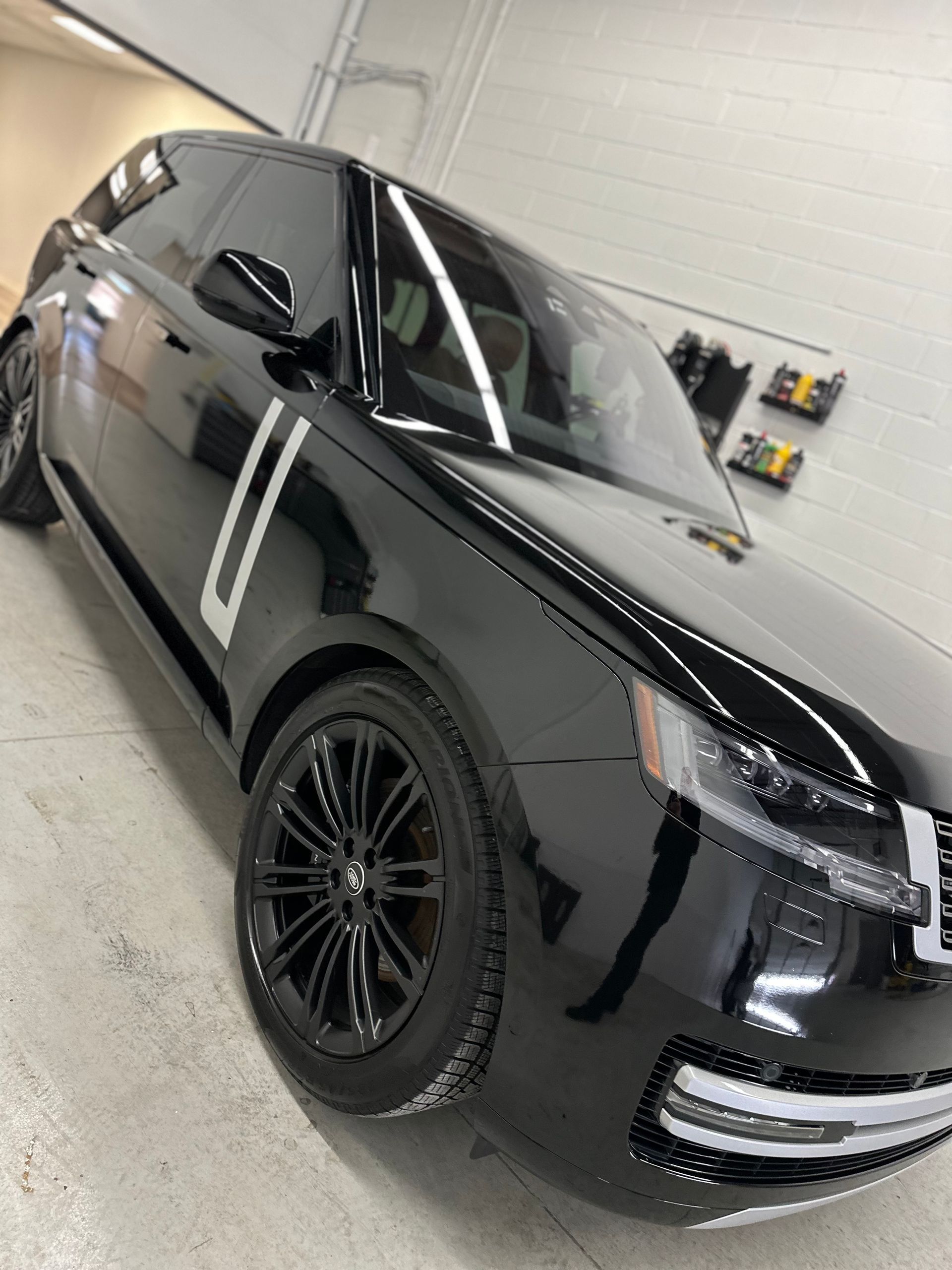 A sleek black Range Rover parked in a brightly lit indoor garage, featuring glossy paint and black rims.