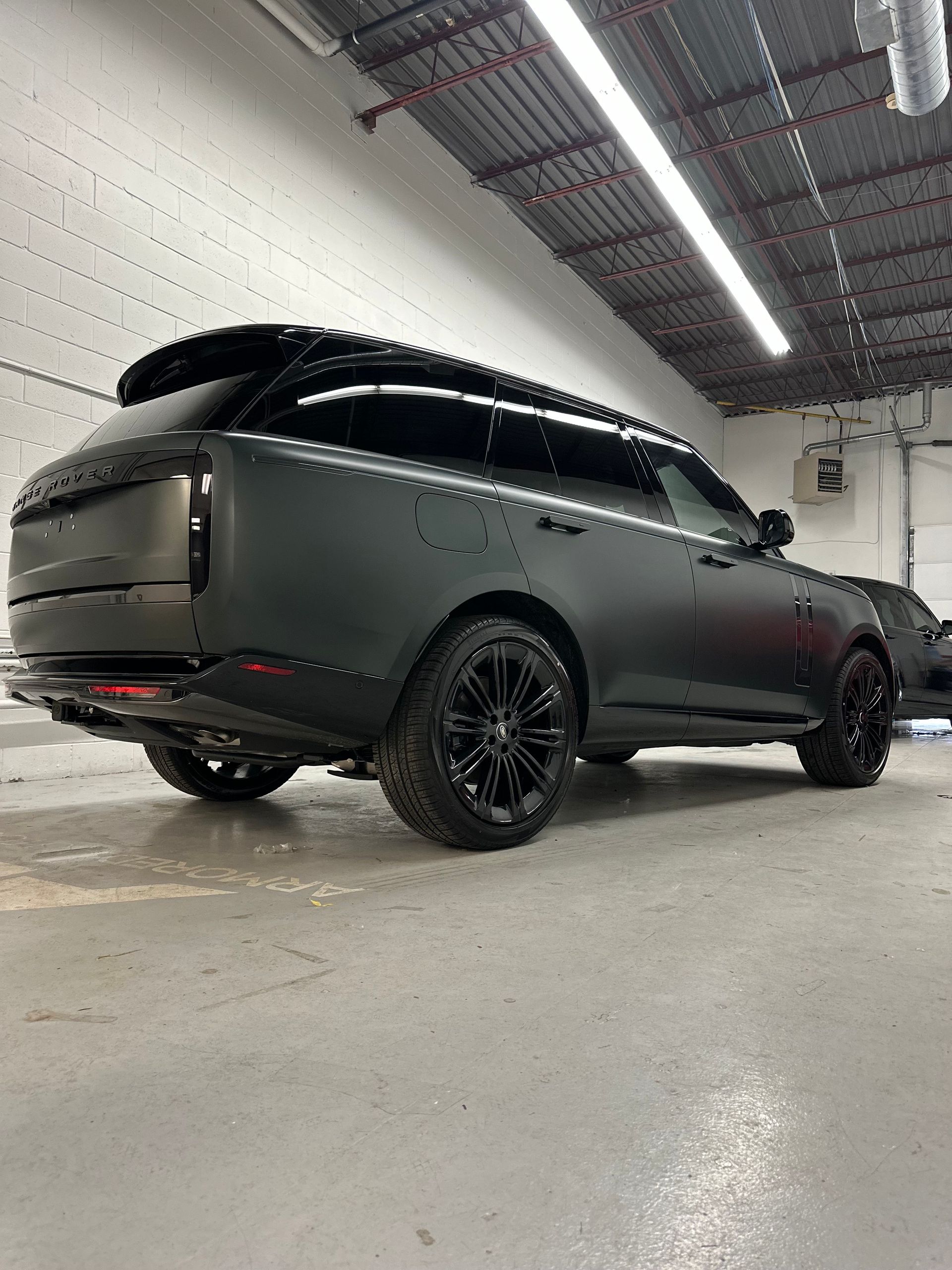 A matte black Range Rover SUV parked in a garage with industrial lighting overhead.