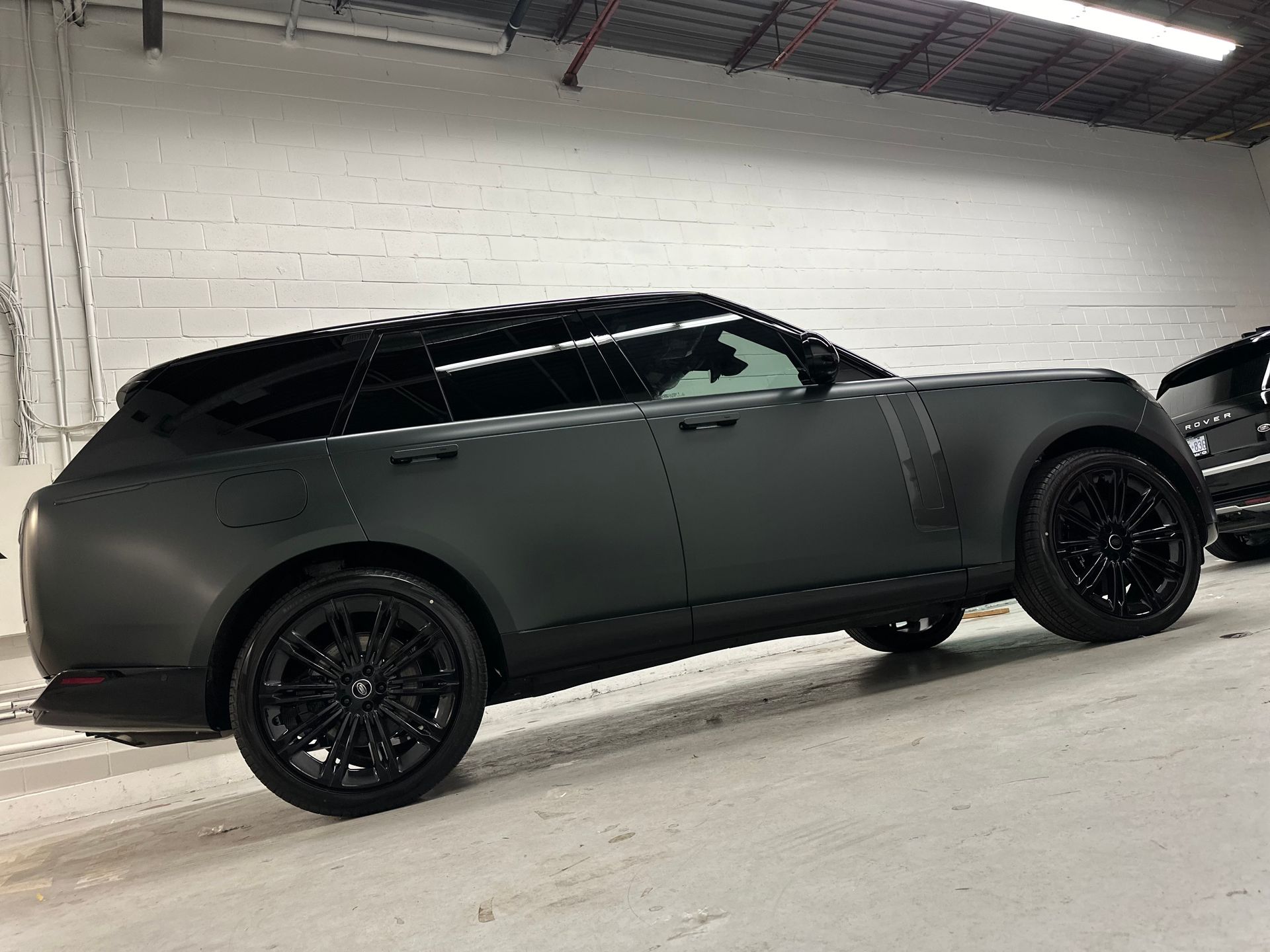 A matte black Range Rover SUV parked inside a garage with white brick walls.