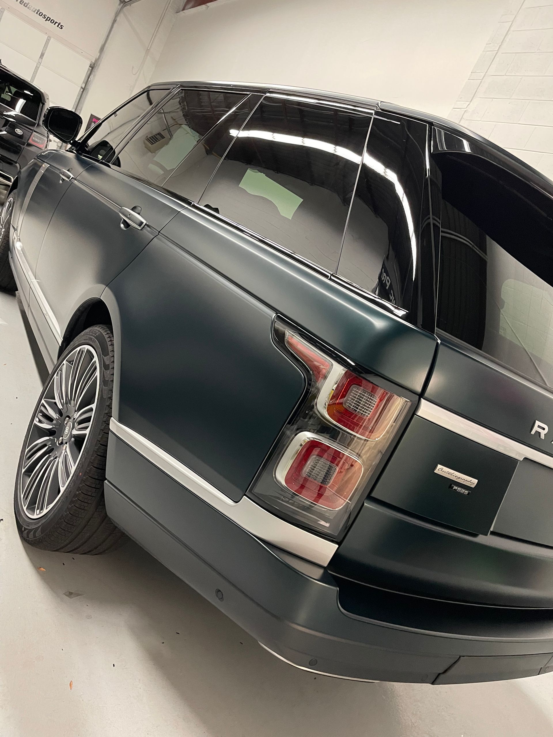 A dark green, matte-finish Range Rover parked inside a garage, showing its rear tail light and alloy wheel.