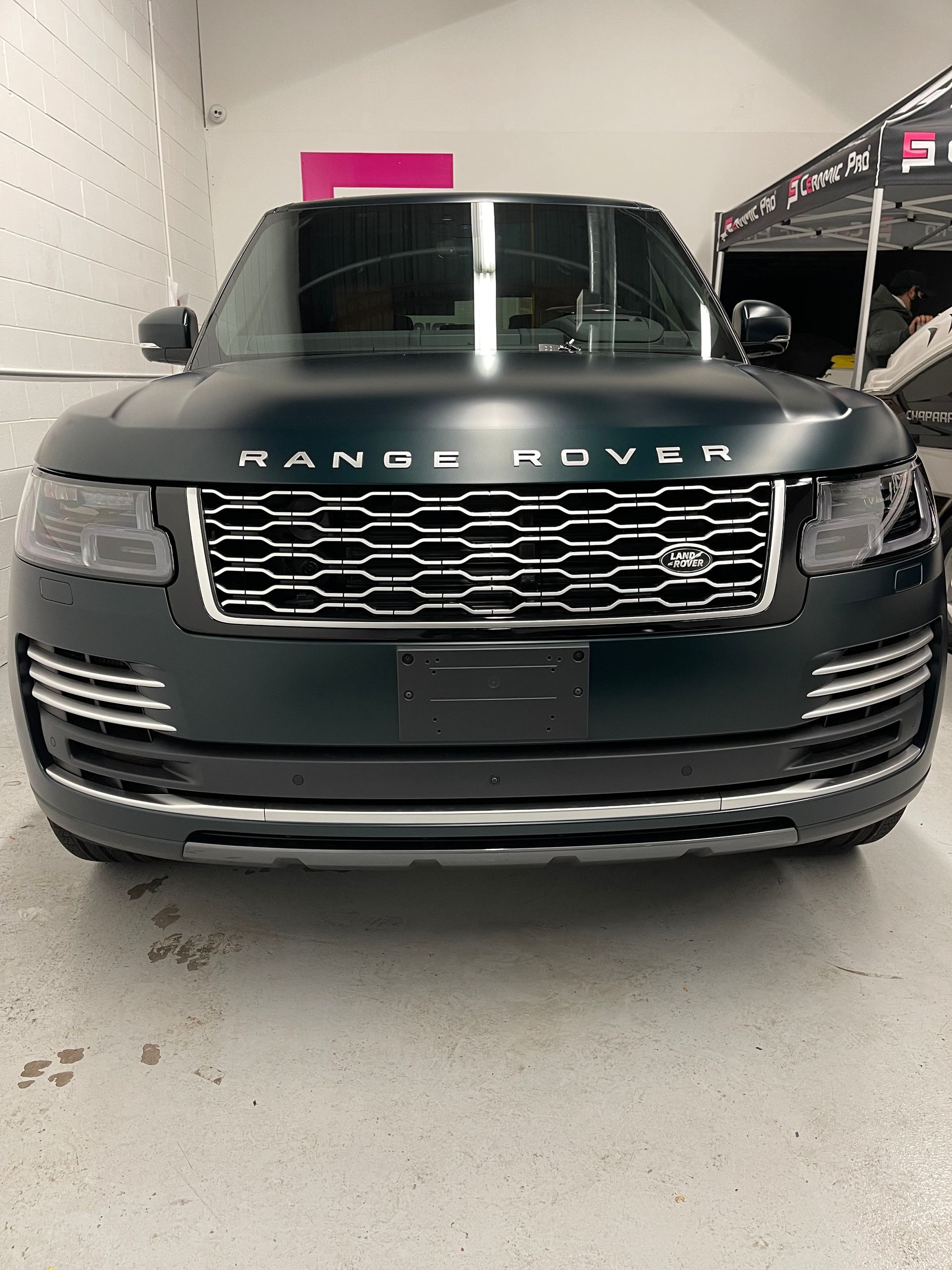 Front view of a matte-finish green Range Rover parked inside an automotive workshop.