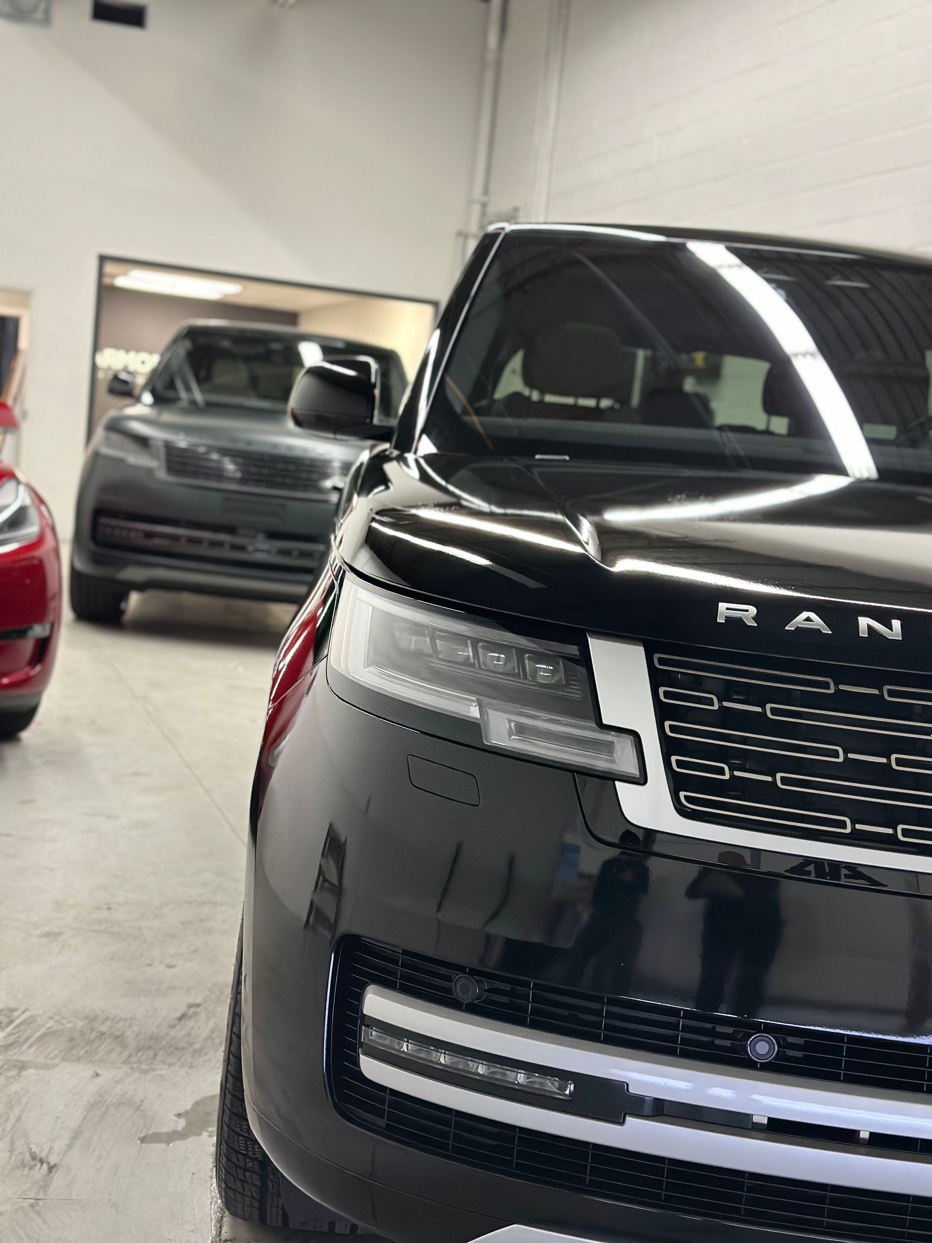 A close-up view of the front of a black Range Rover, with another vehicle parked in the background of a garage.
