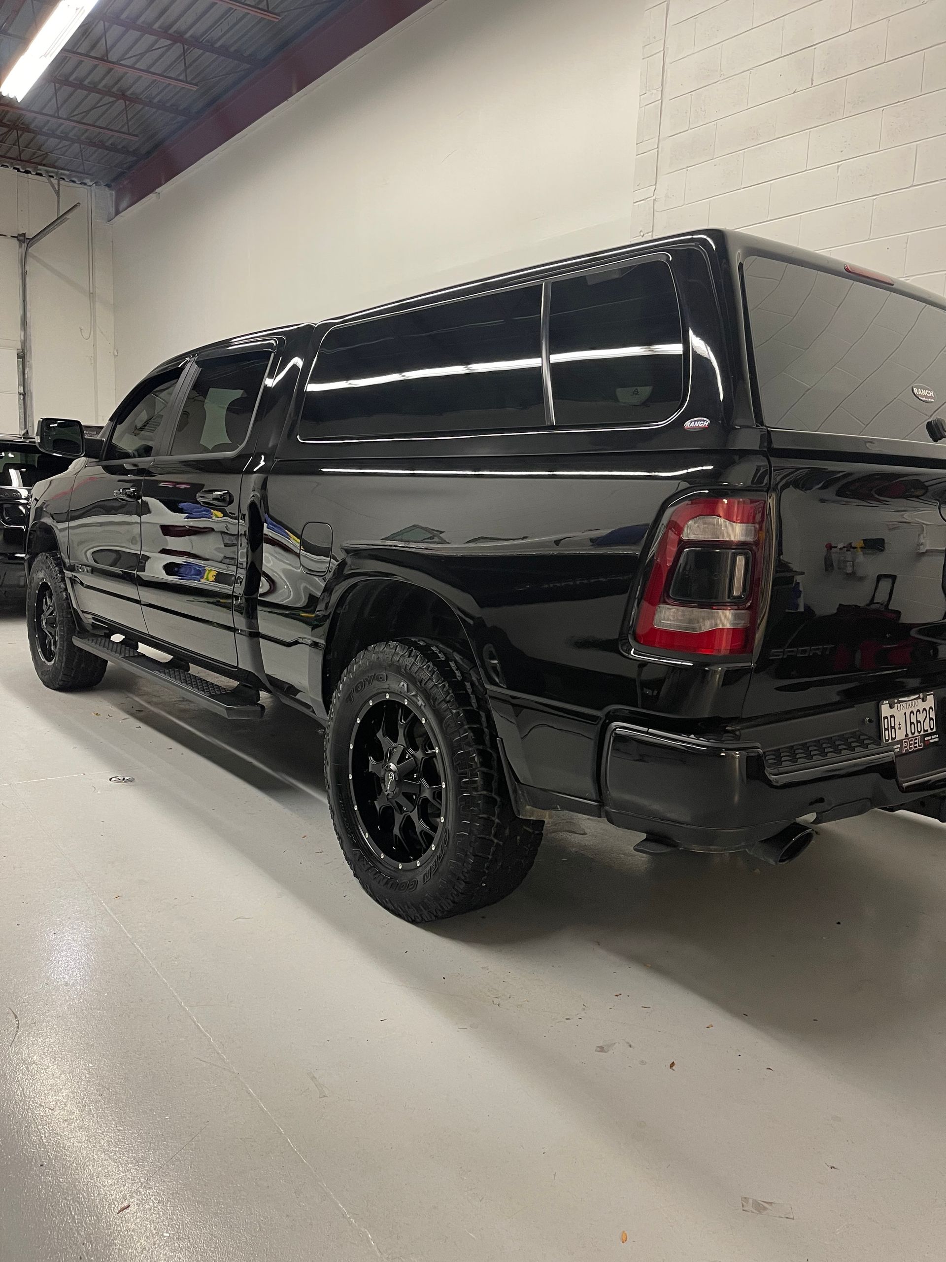 A black pickup truck with a camper shell parked inside a garage with a bright overhead light.