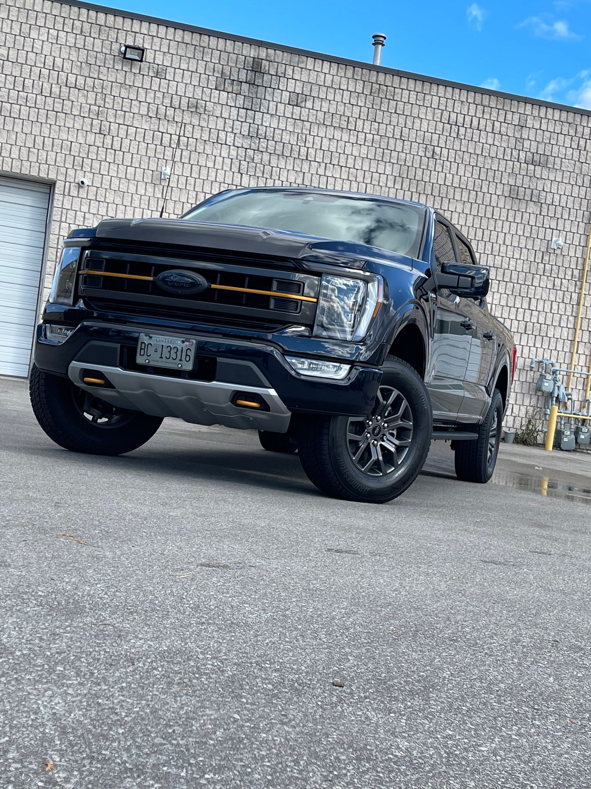 A black Ford F-150 Tremor parked on an asphalt lot in front of a building with a textured, light-colored wall.