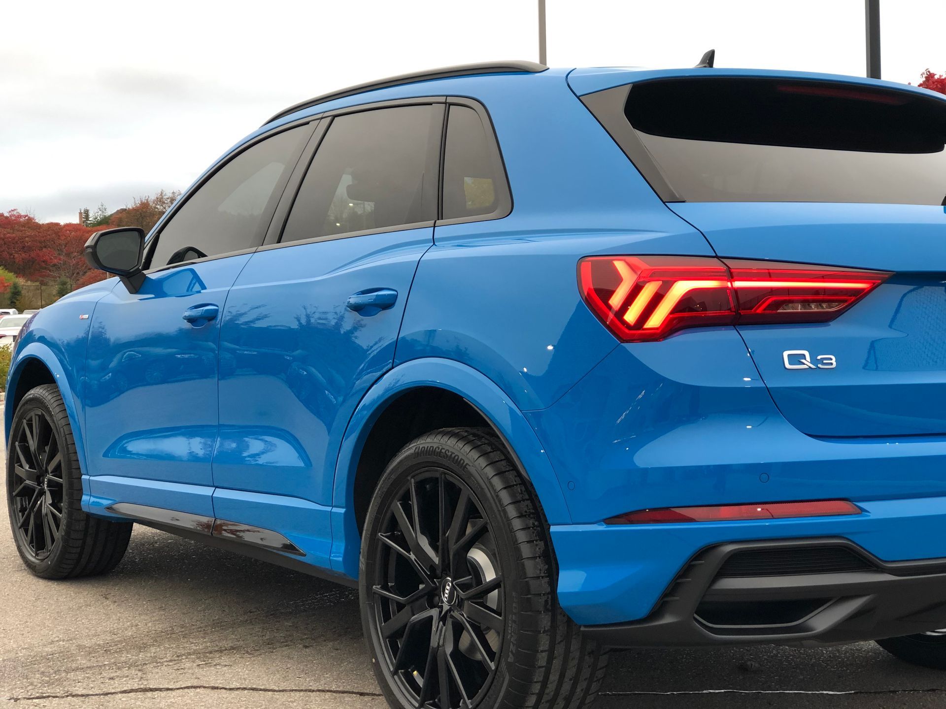 A bright blue Audi Q3 SUV with black wheels parked outside on an overcast day.