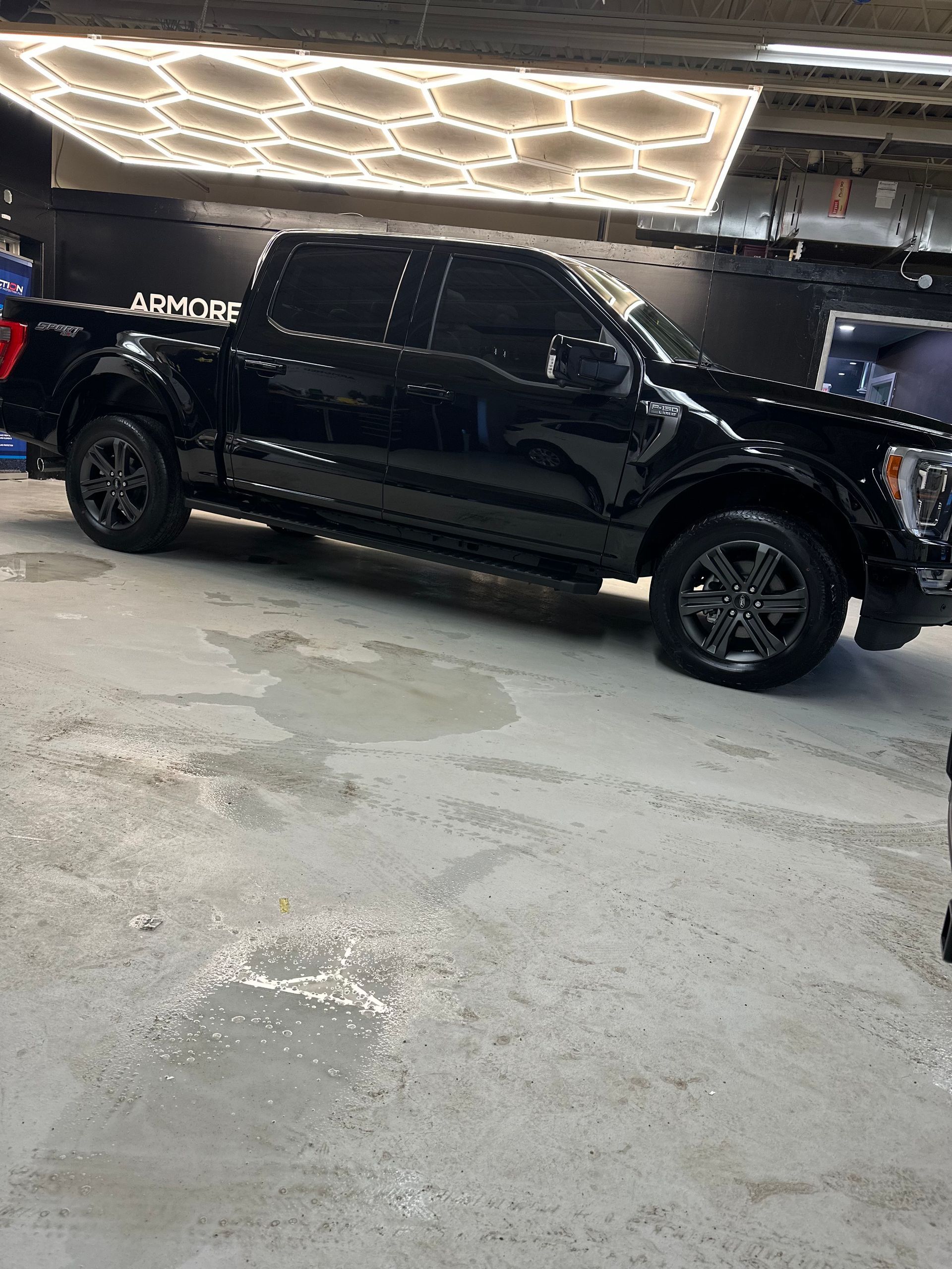 A black Ford F-150 pickup truck parked inside a garage with hexagon-patterned overhead lighting.