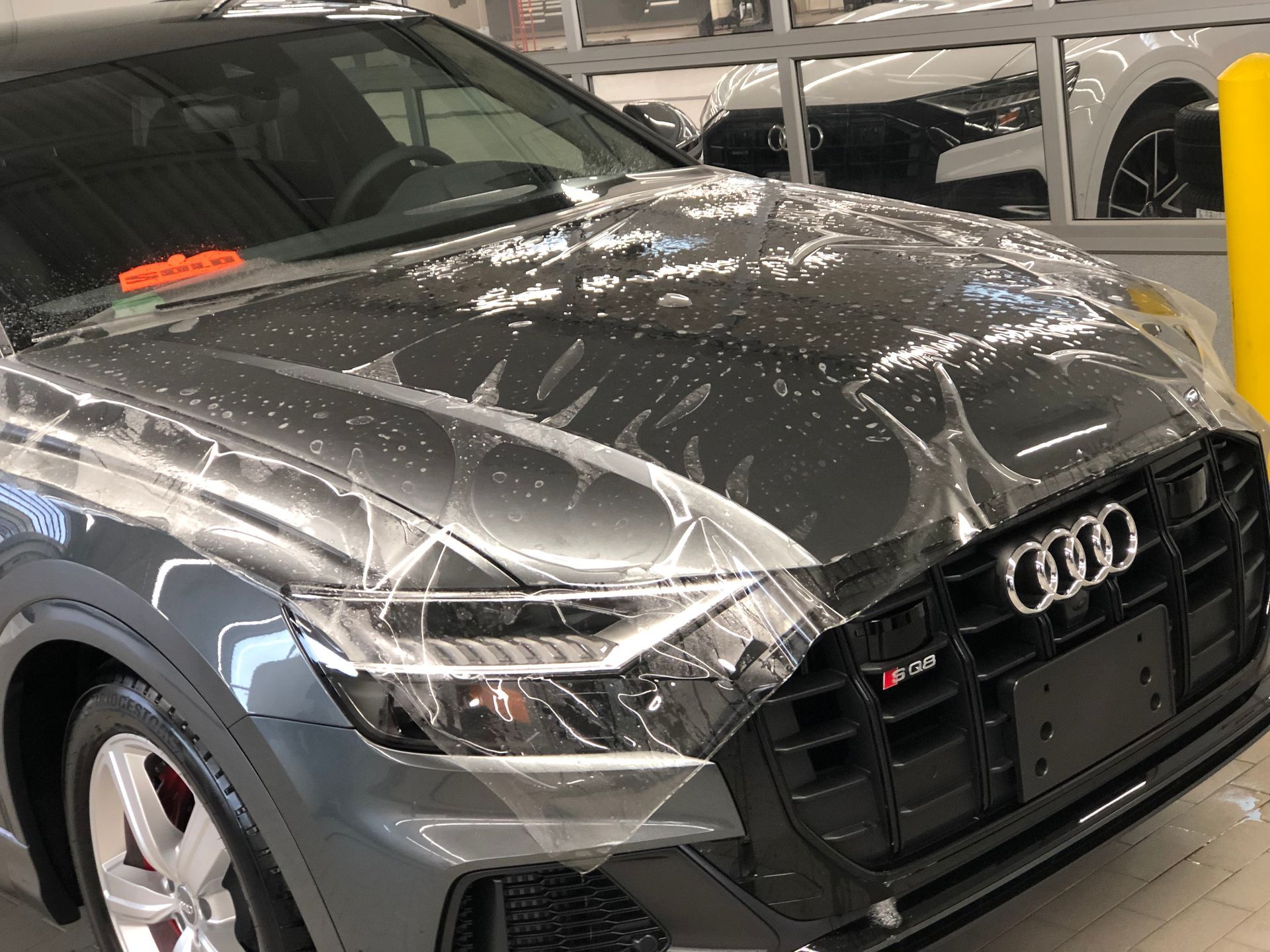 A dark gray Audi SQ8 SUV with protective plastic film partially covering its hood and headlight in a dealership.