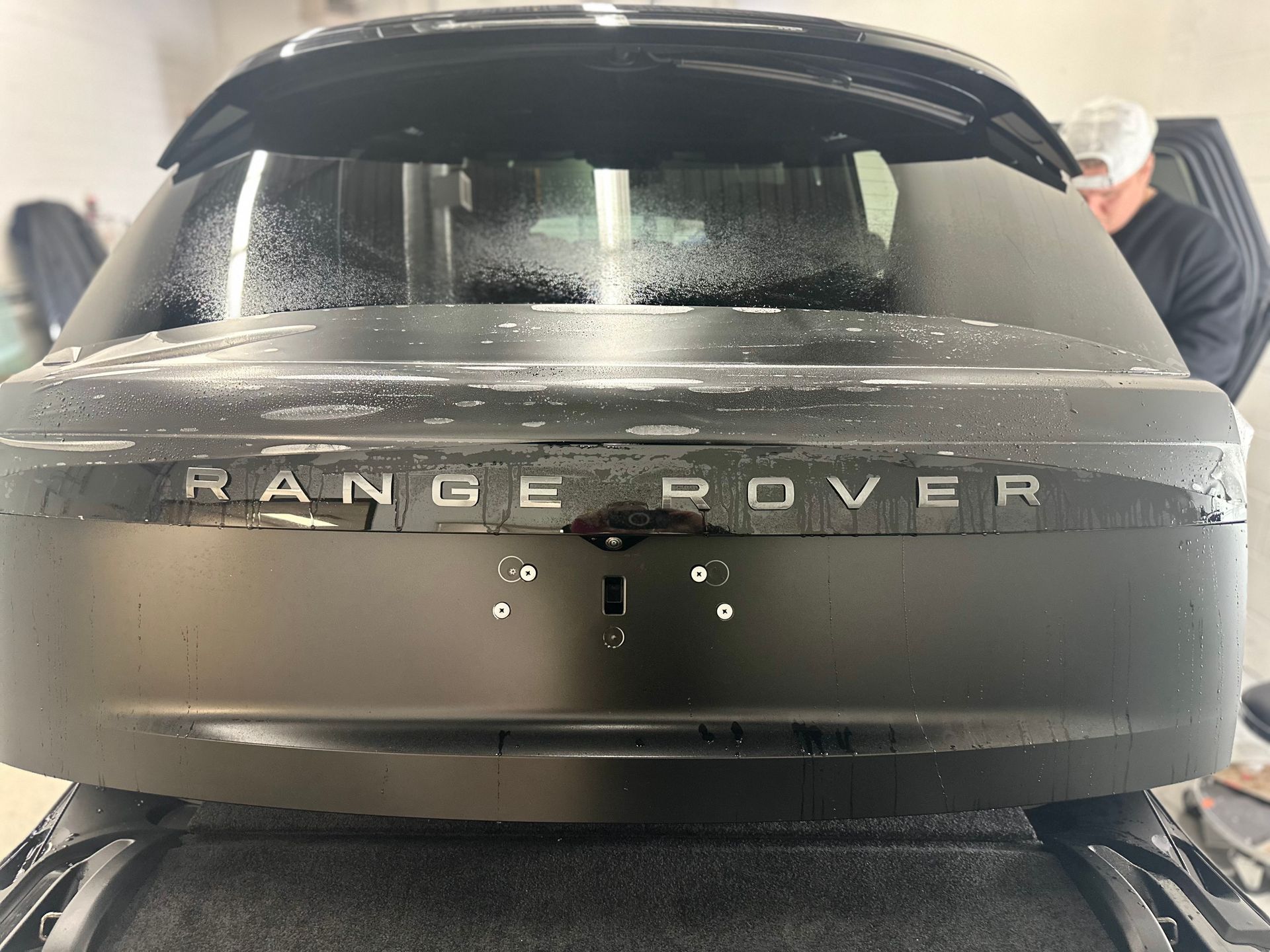 A close-up view of the rear of a matte black Range Rover being prepared with a wet film application.