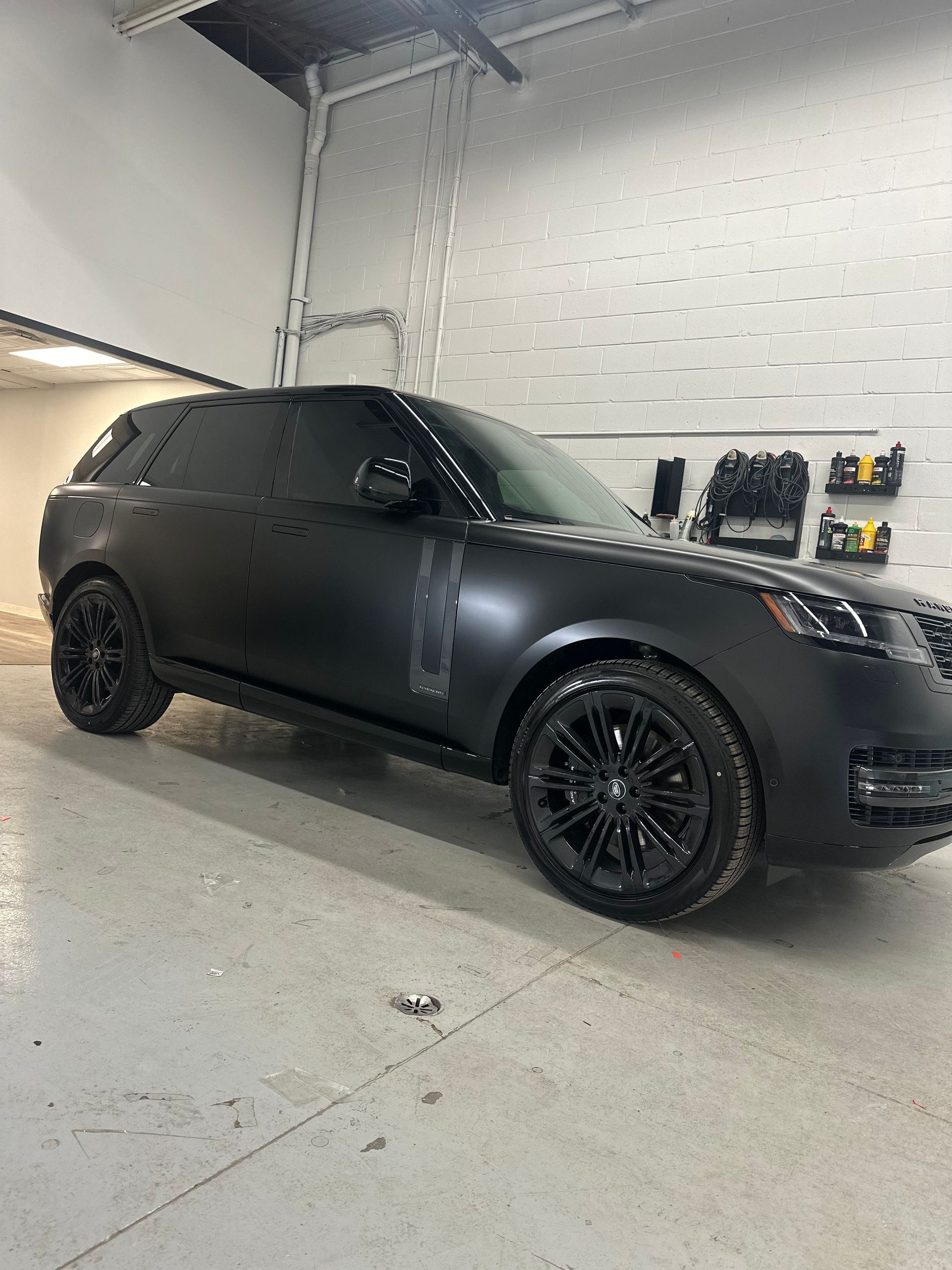 A matte black Range Rover SUV parked inside a workshop with concrete floors and white walls.