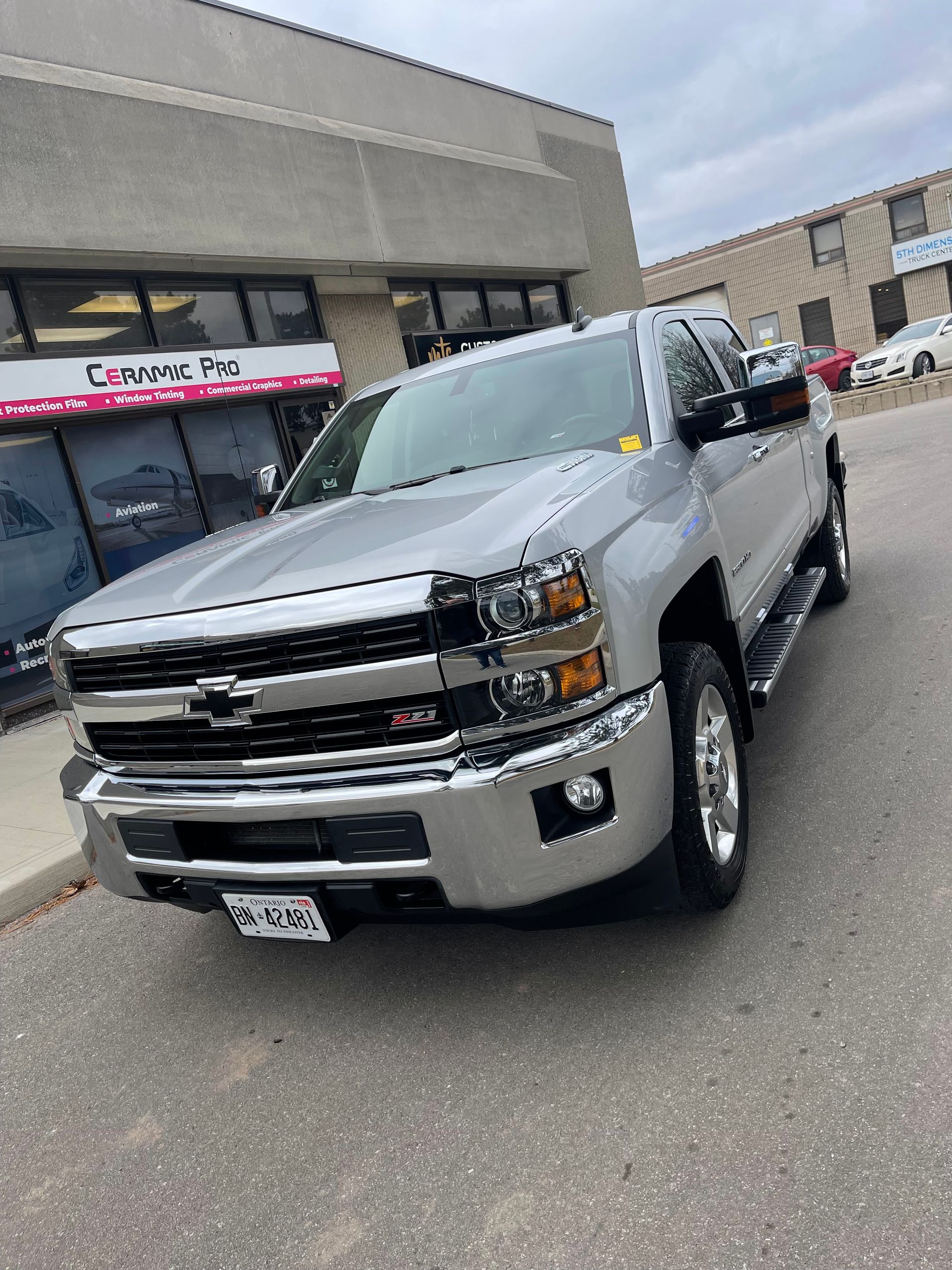 A silver Chevrolet Silverado pickup truck parked in front of a commercial building on a cloudy day.
