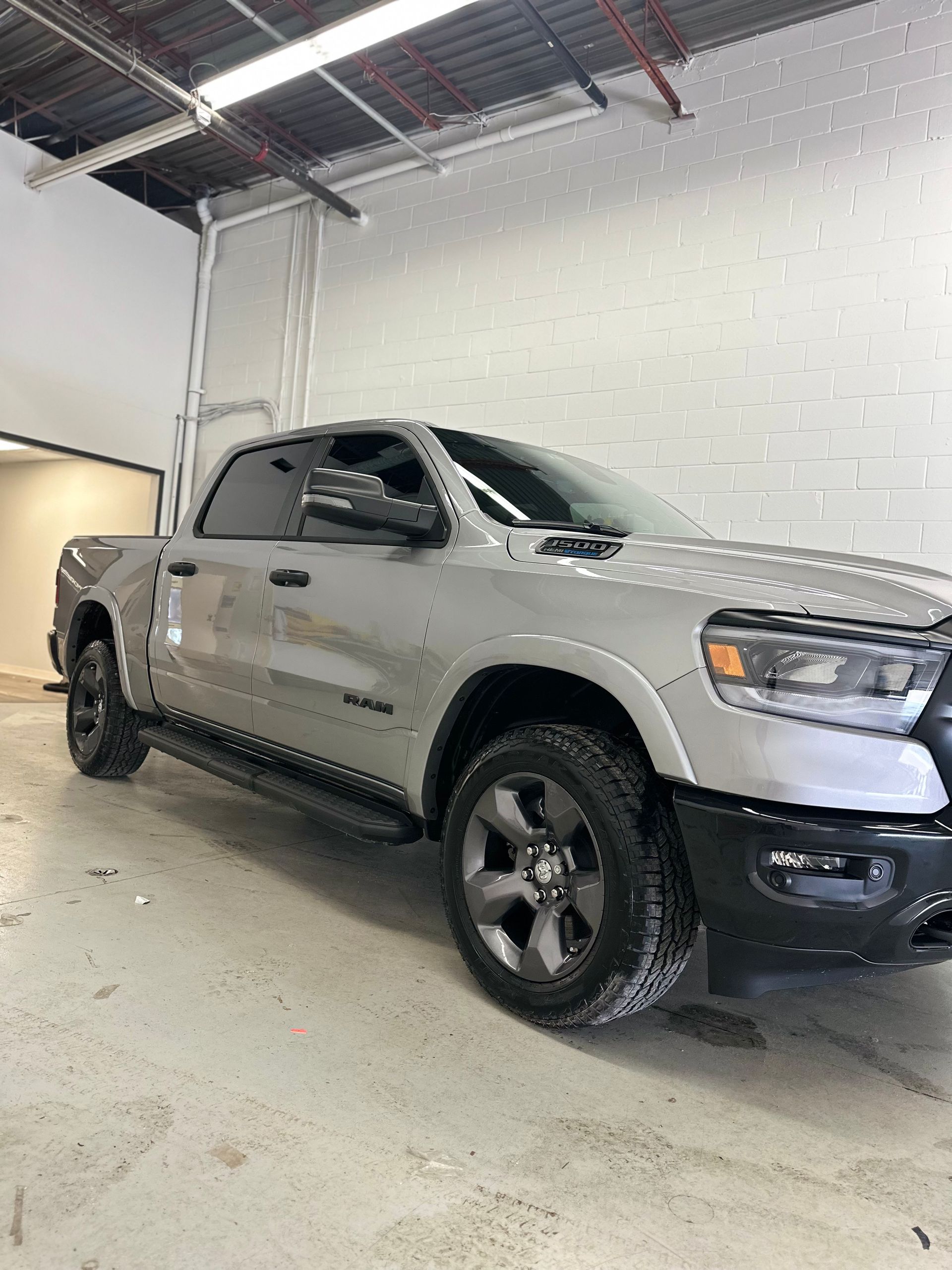 A grey Ram pickup truck parked in a well-lit, industrial-style garage with white brick walls.