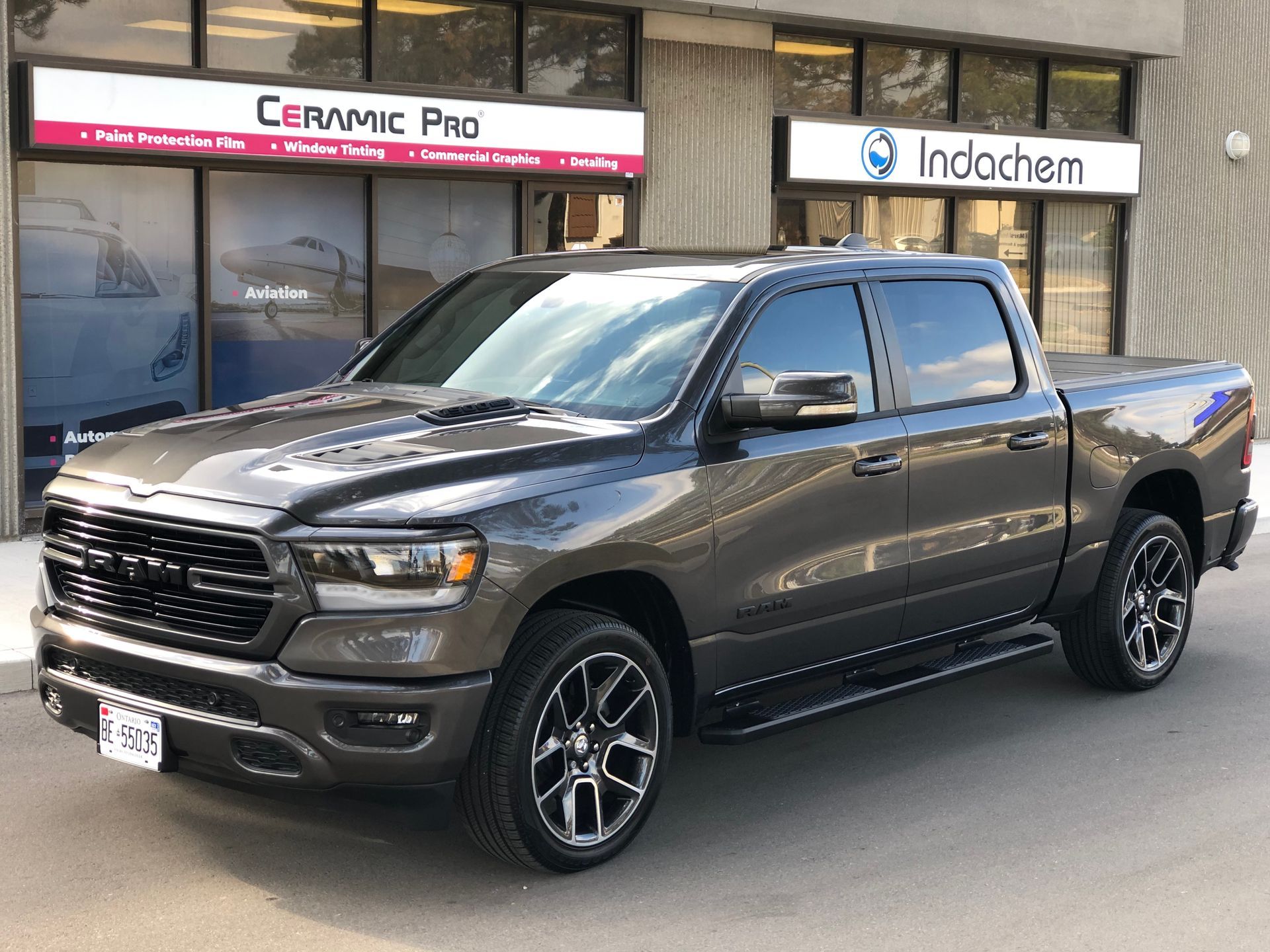 A dark gray Ram pickup truck parked in front of a Ceramic Pro and Indochem business building.